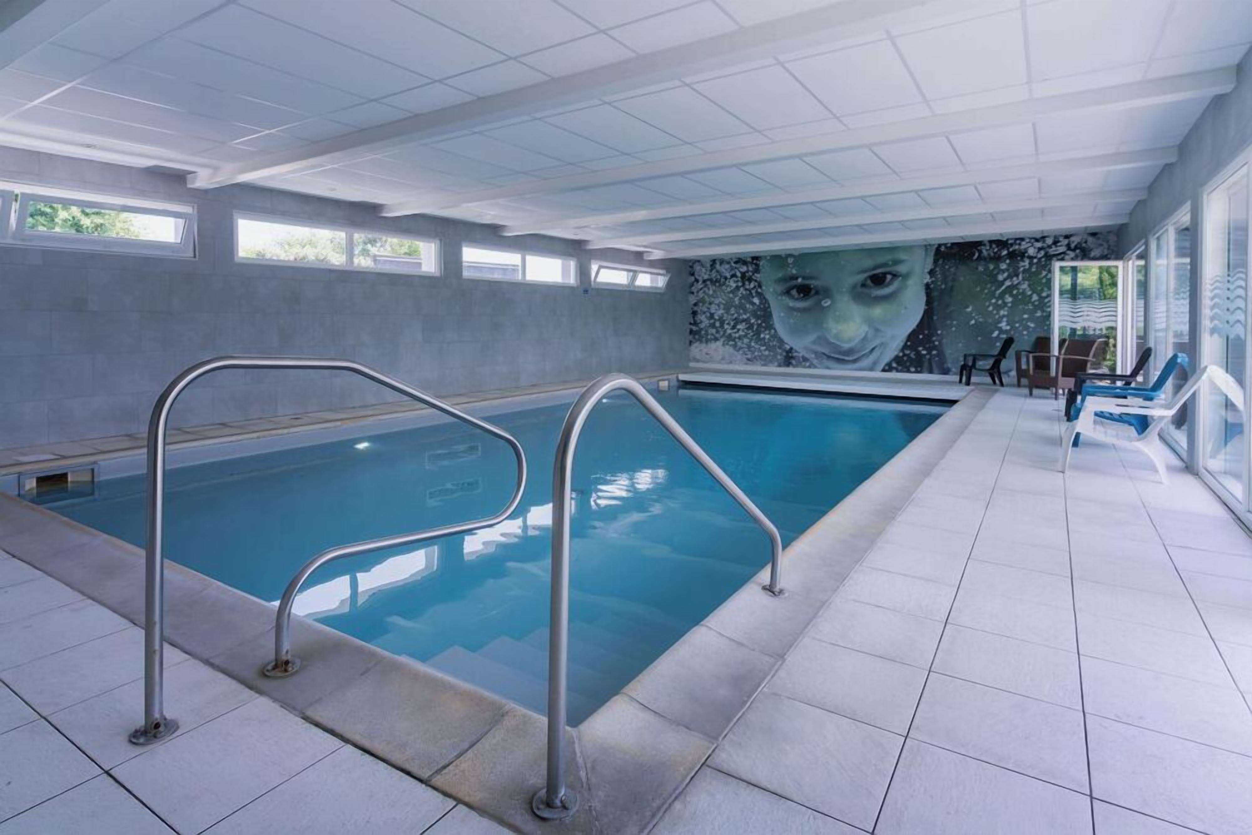 An indoor swimming pool with clear water, metal railings, and a mural on the wall.