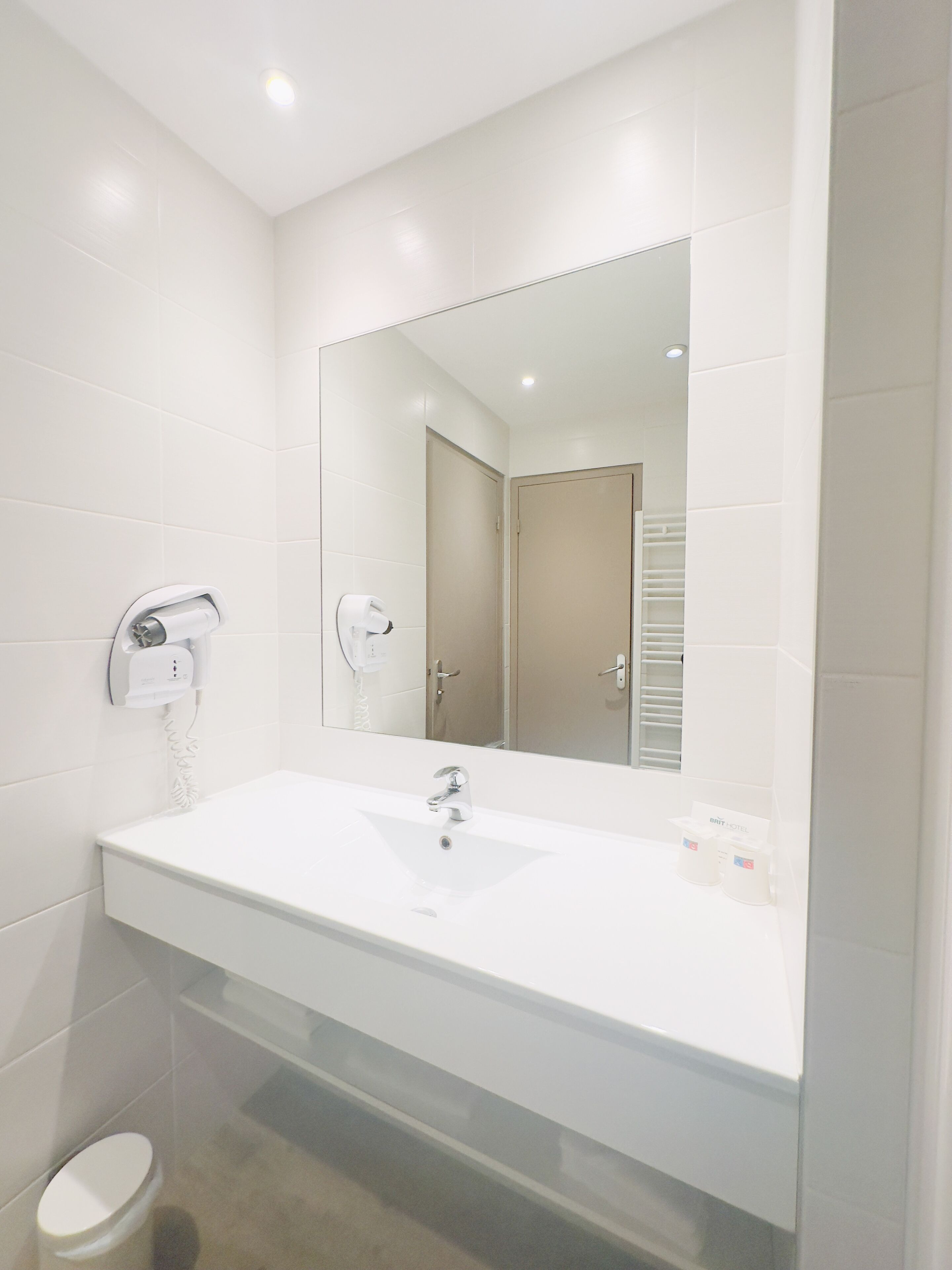 Un baño moderno con un lavamanos blanco, un espejo y un secador de pelo montado en la pared.