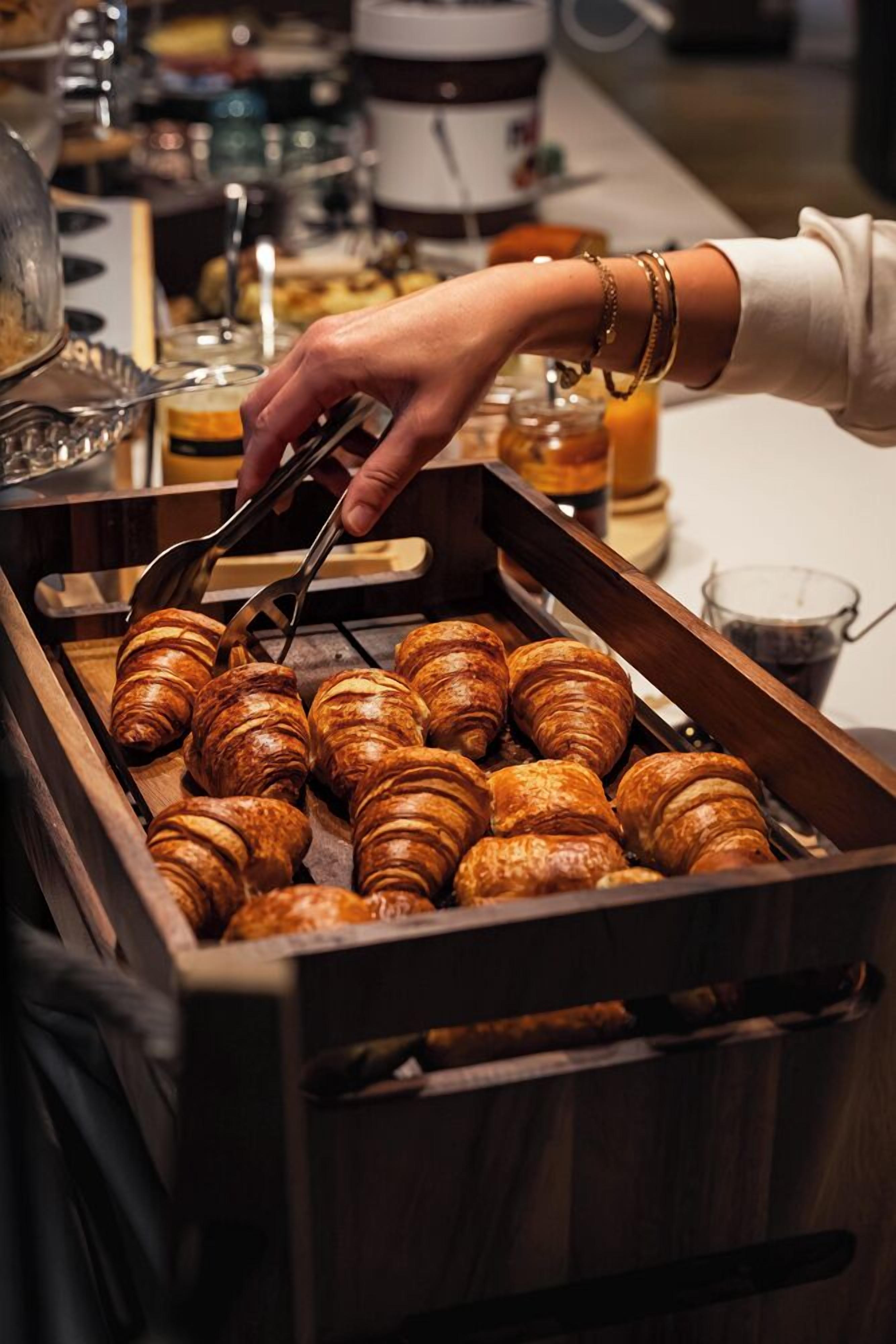 Une main tendue vers des croissants disposés sur un plateau en bois.