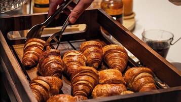 Une main tendue vers des croissants disposés sur un plateau en bois.
