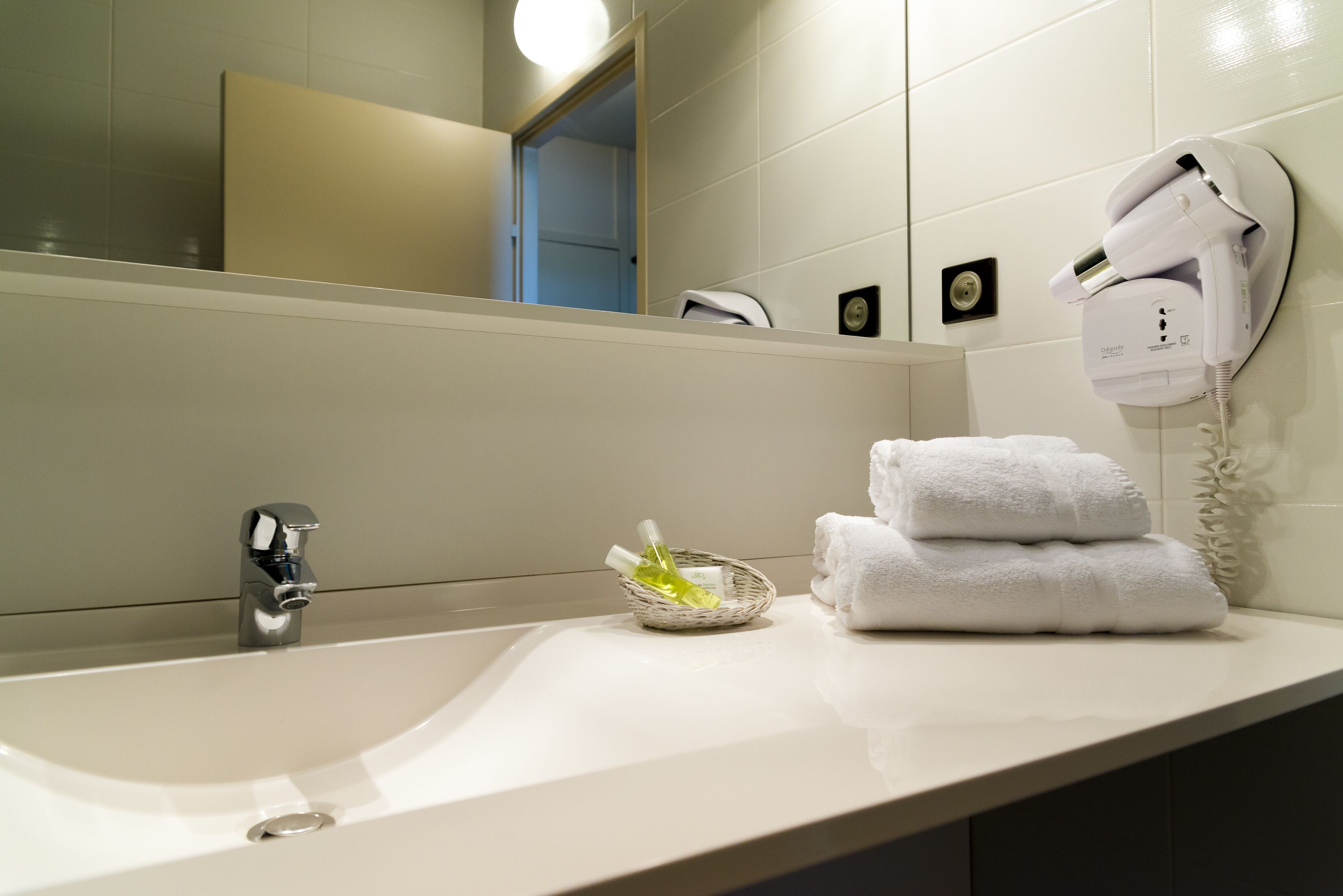 Une salle de bain équipée d’un lavabo, d’un miroir, d’un sèche-cheveux et d’un porte-serviettes.