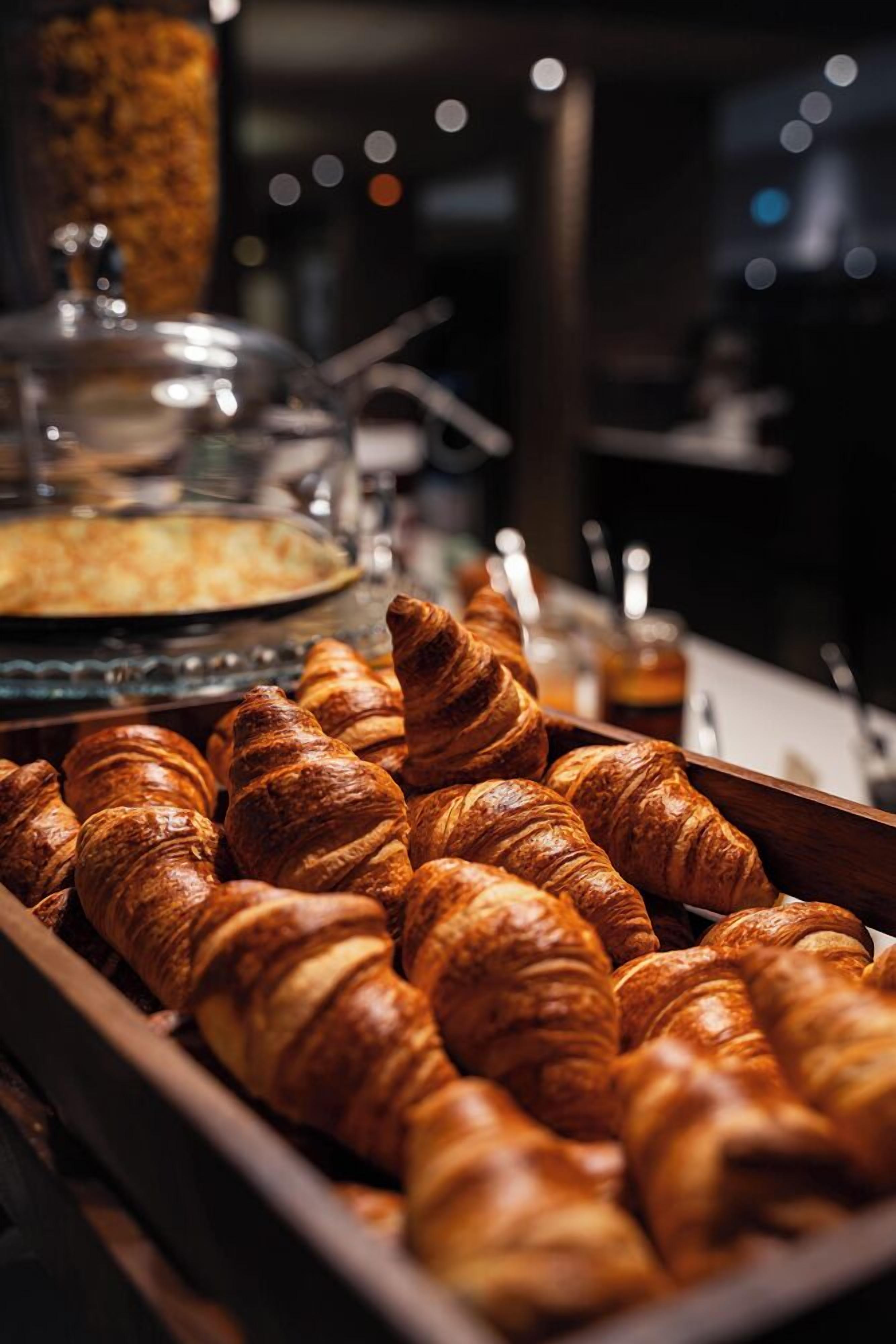 Un bufé con croissants y un recipiente tapado, probablemente con alimentos para el desayuno.