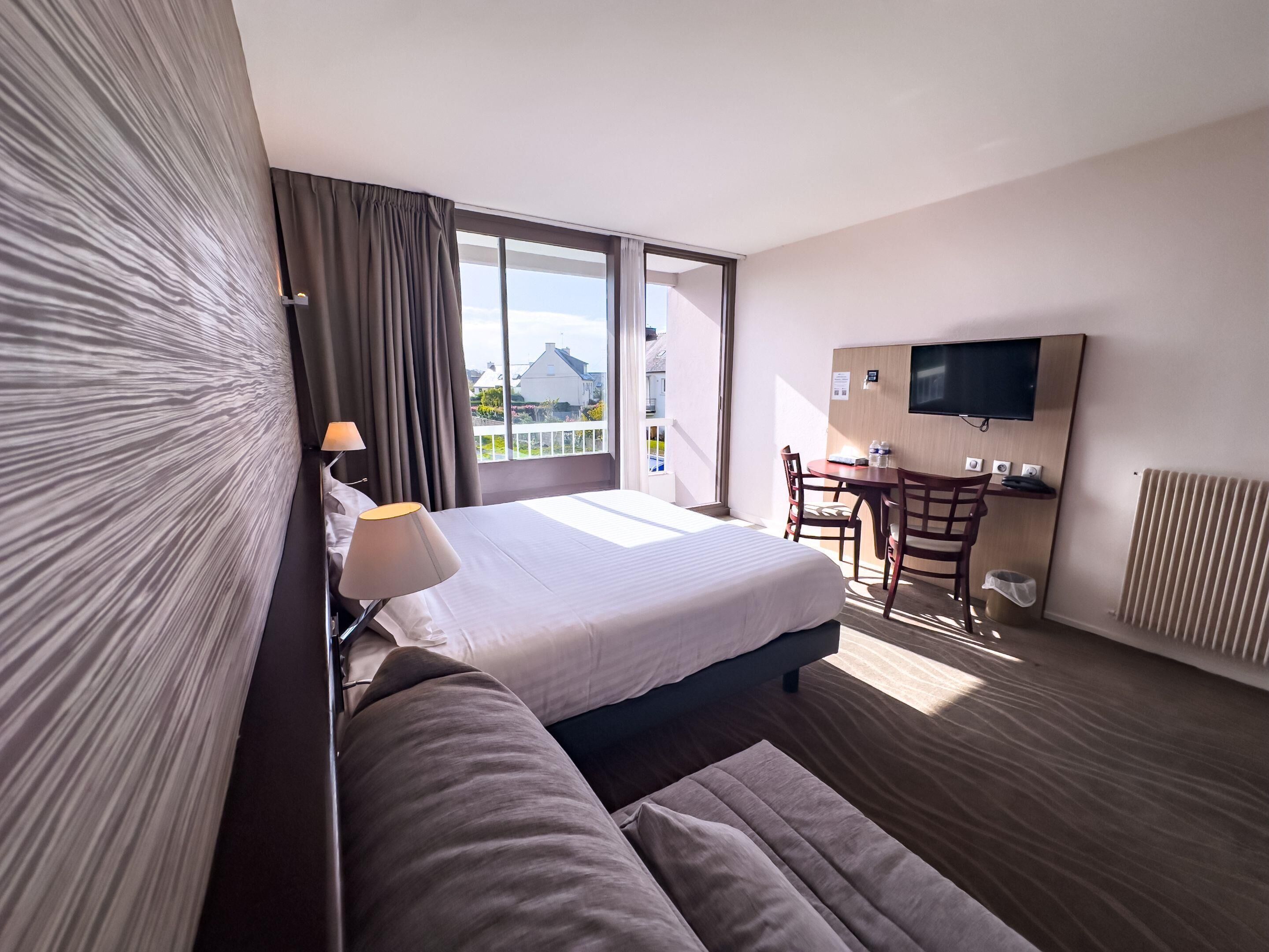 Una habitación de hotel con una cama, un escritorio, un televisor y vistas al exterior.