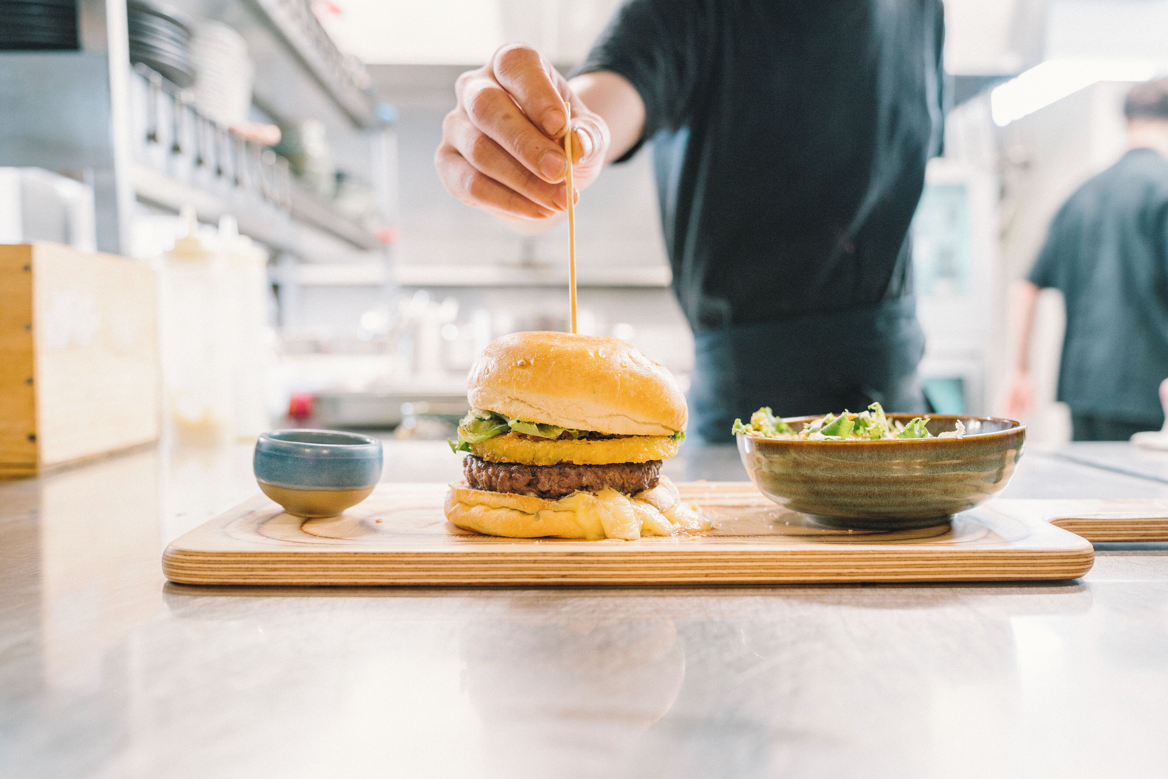 En burger på en træplanke med en salatskål ved siden af.