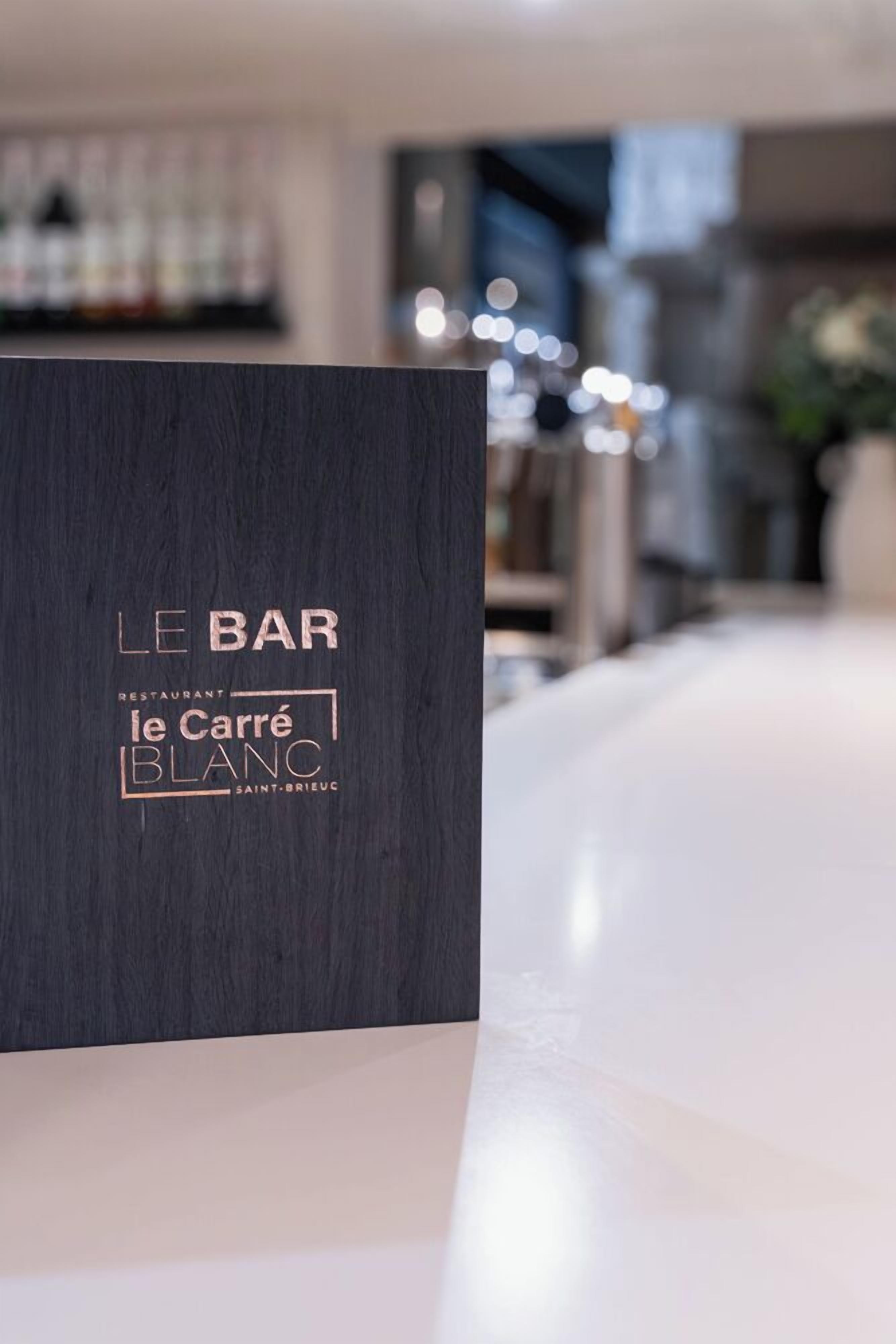 Un mostrador de recepción de madera oscura con el texto "LE BAR le Carré BLANC SAINT-BREUC".