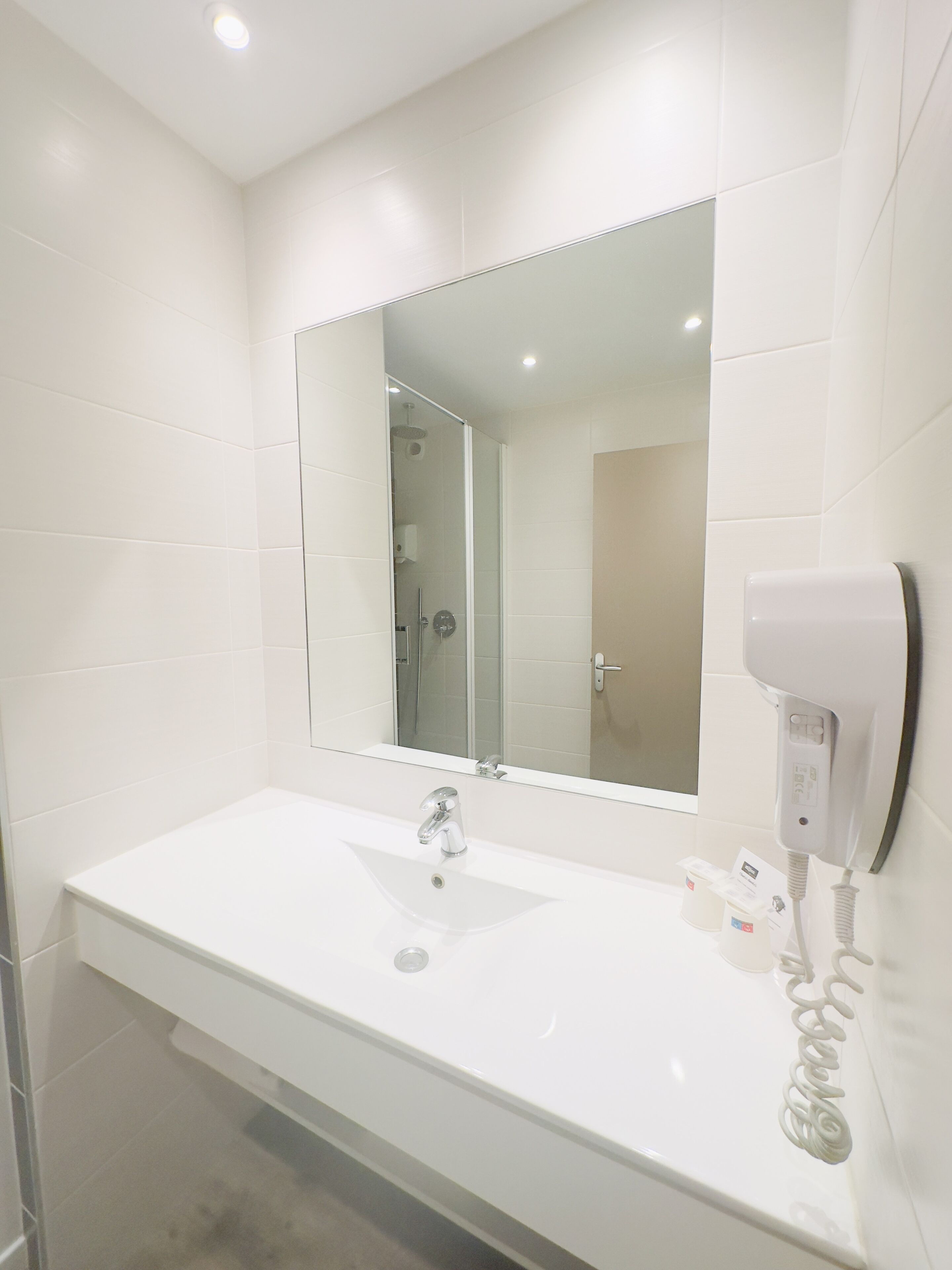 Un bagno moderno con un lavandino bianco, uno specchio grande e un asciugacapelli fissato alla parete.