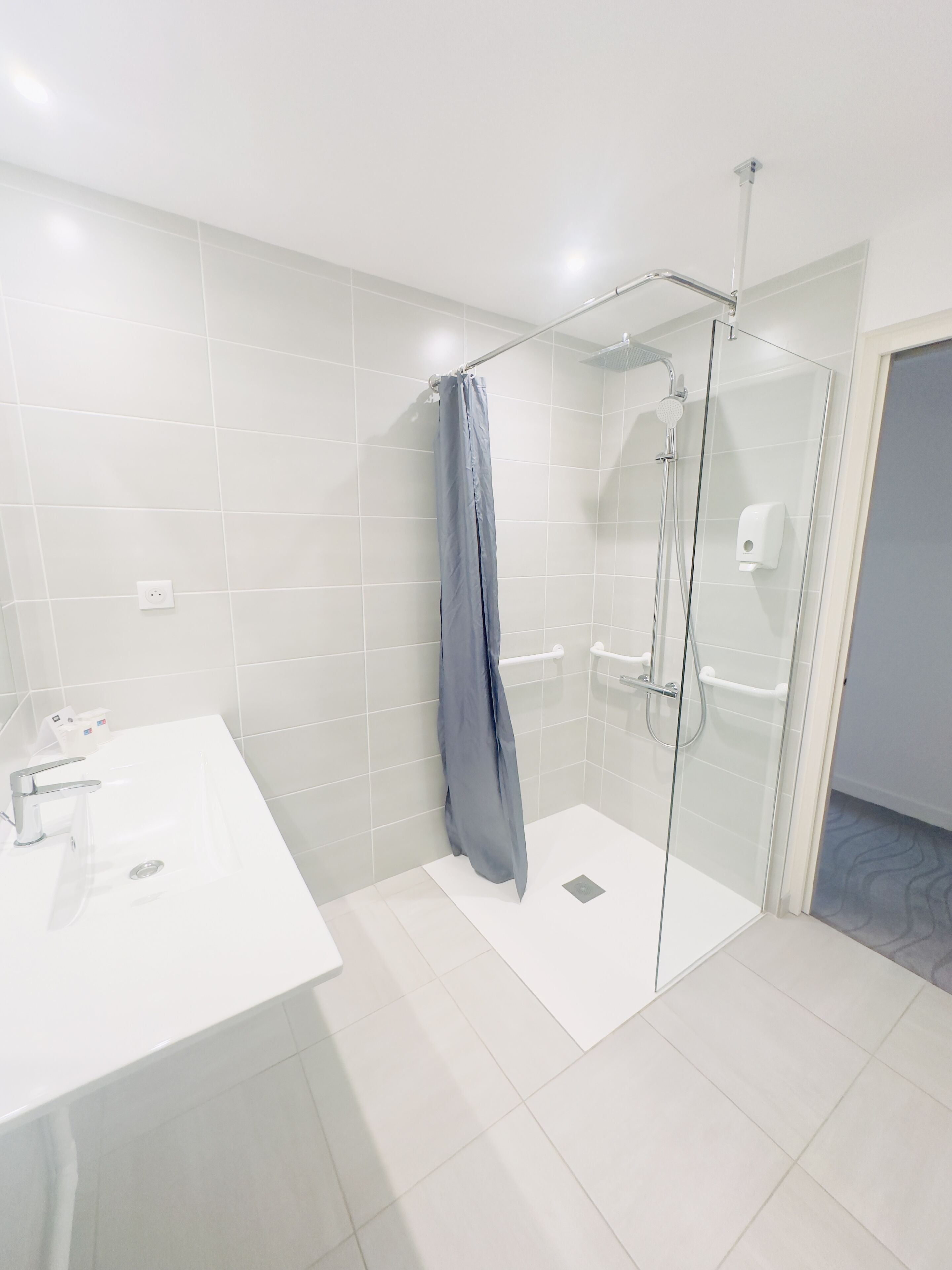 Une salle de bain moderne avec une douche à l’italienne en verre, un lavabo blanc et un sol carrelé de couleur blanche.