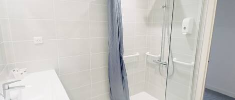 Une salle de bain moderne avec une douche à l’italienne en verre, un lavabo blanc et un sol carrelé de couleur blanche.
