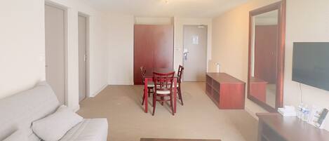 Una sala de estar con un sofá, una mesa de centro de madera, una mesa de comedor con sillas, un televisor y un espejo.