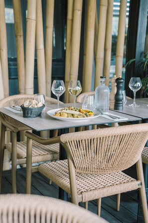 A dining table set with plates, glasses, and a basket of bread, surrounded by wicker chairs. - Brit Hotel Saint Brieuc (Langueux)