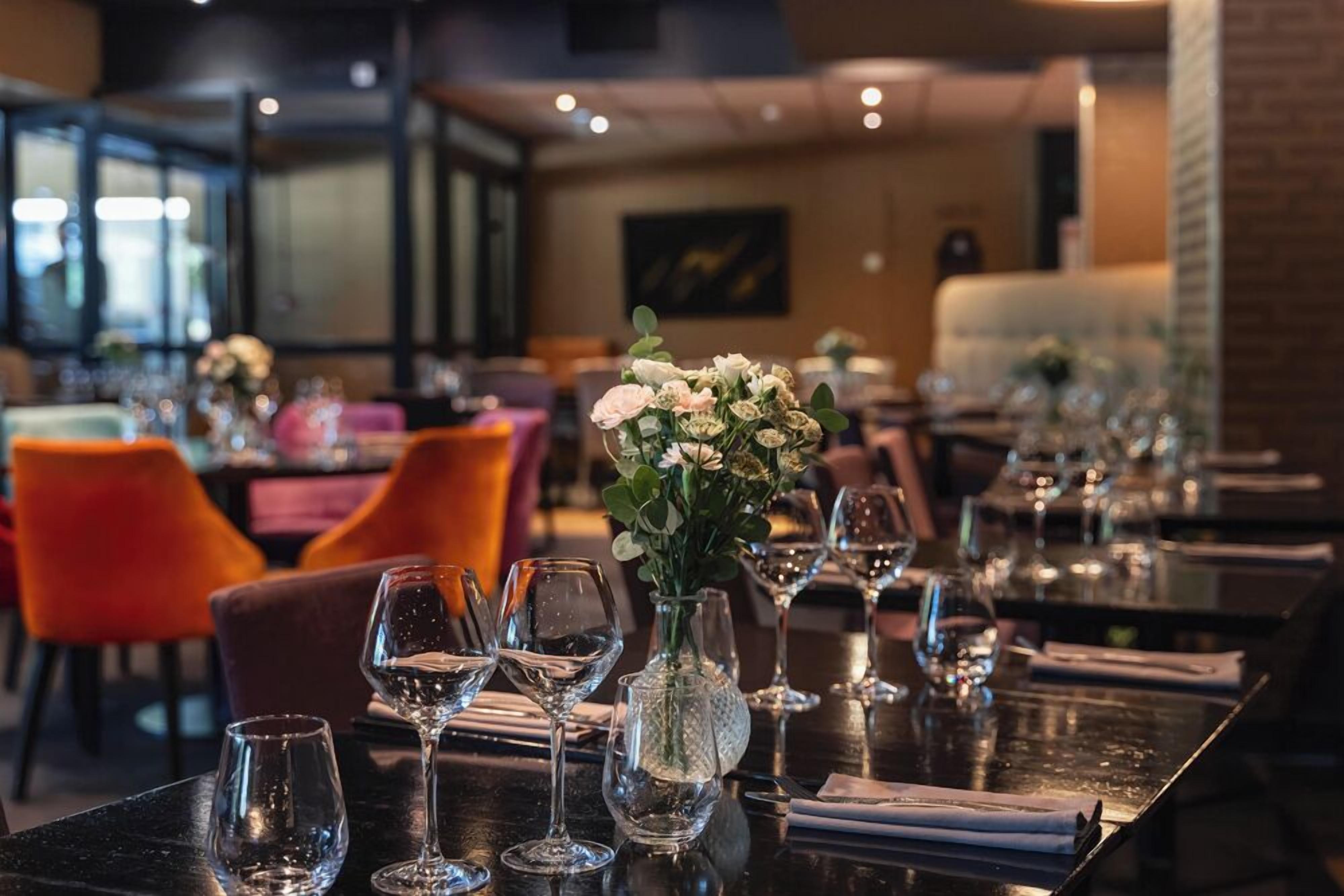Interior de restaurante con mesas dispuestas para comer, con cubertería de vidrio transparente y centros de mesa con flores.
