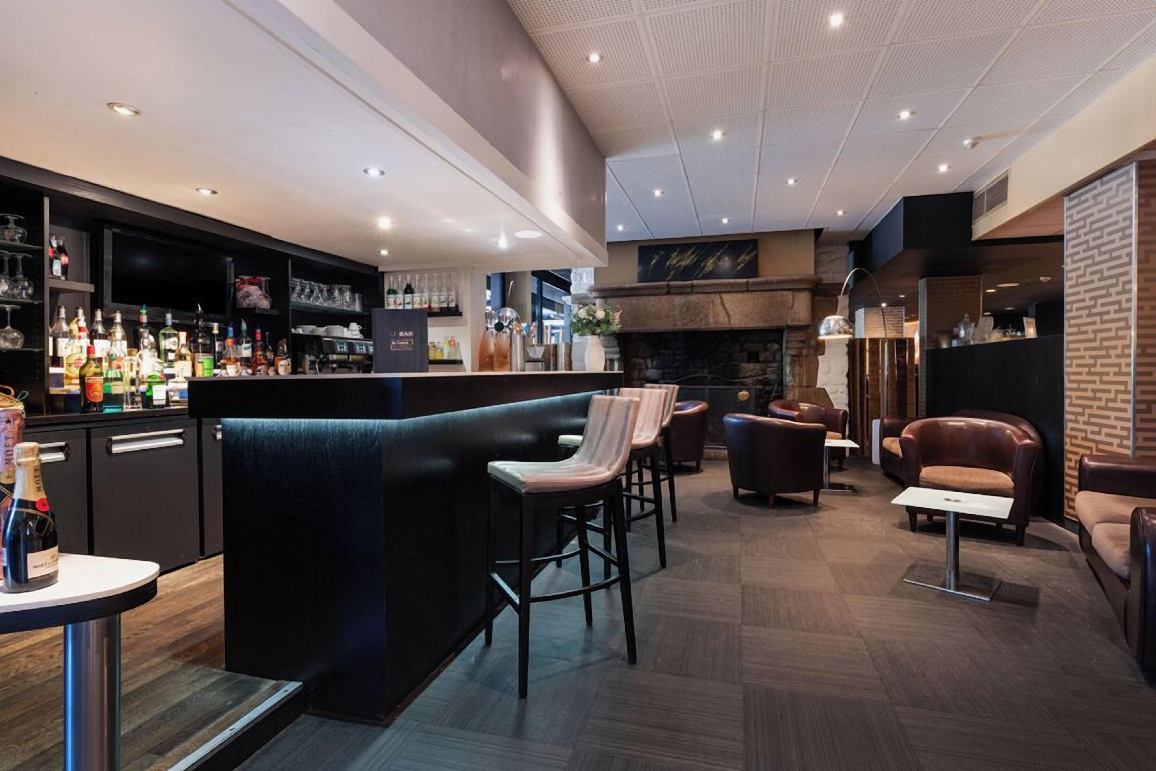 A bar area with stools, a fireplace, and a variety of bottles.