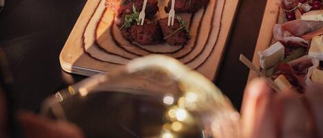 Una tabla de madera con alimentos, un recipiente pequeño de salsa y una copa de vino.