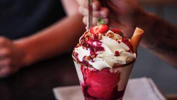 A person holding a dessert with a waffle cone, topped with whipped cream, strawberries, and granola.