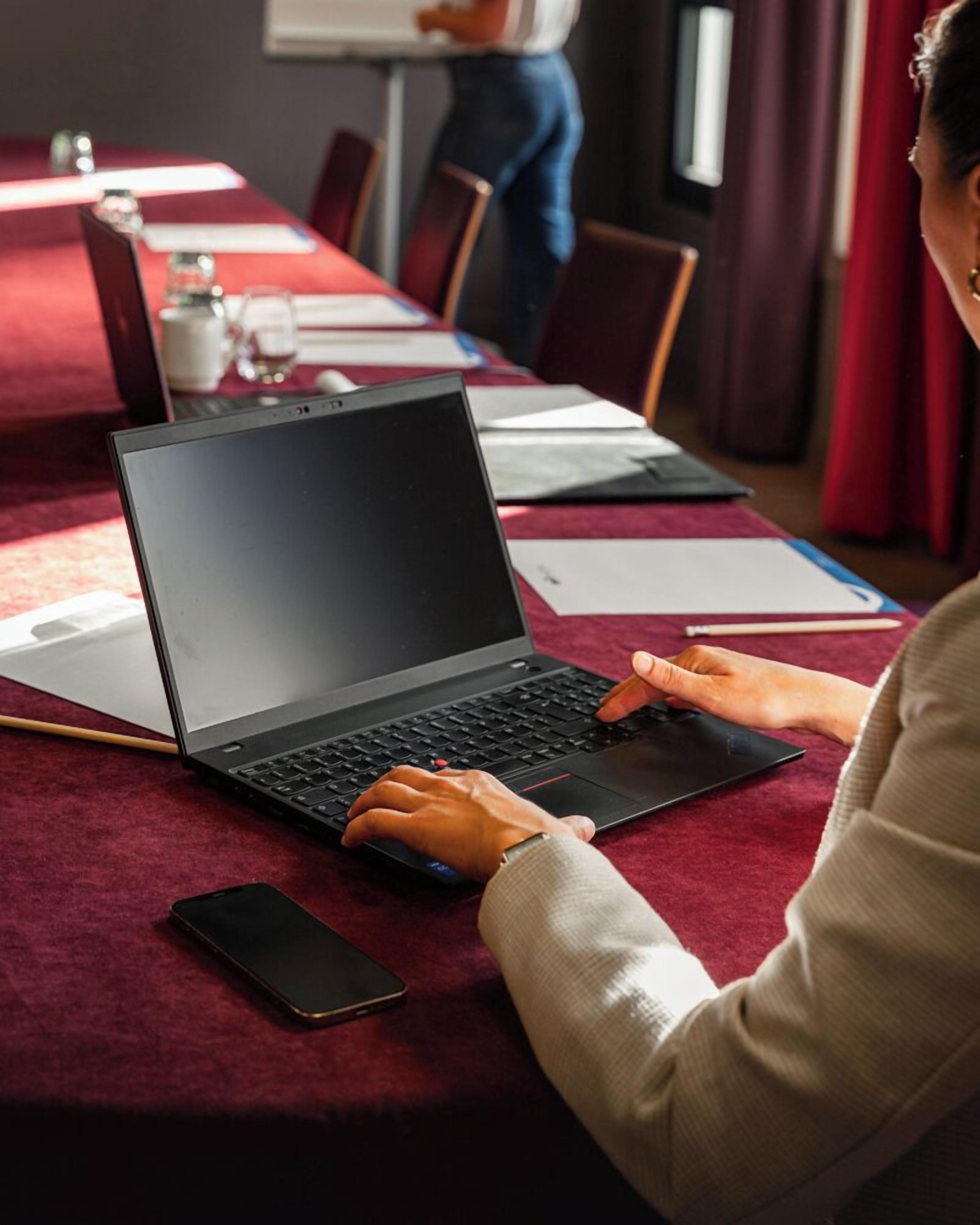 A conference room with a red carpet, a laptop, a smartphone, and a whiteboard in the background.