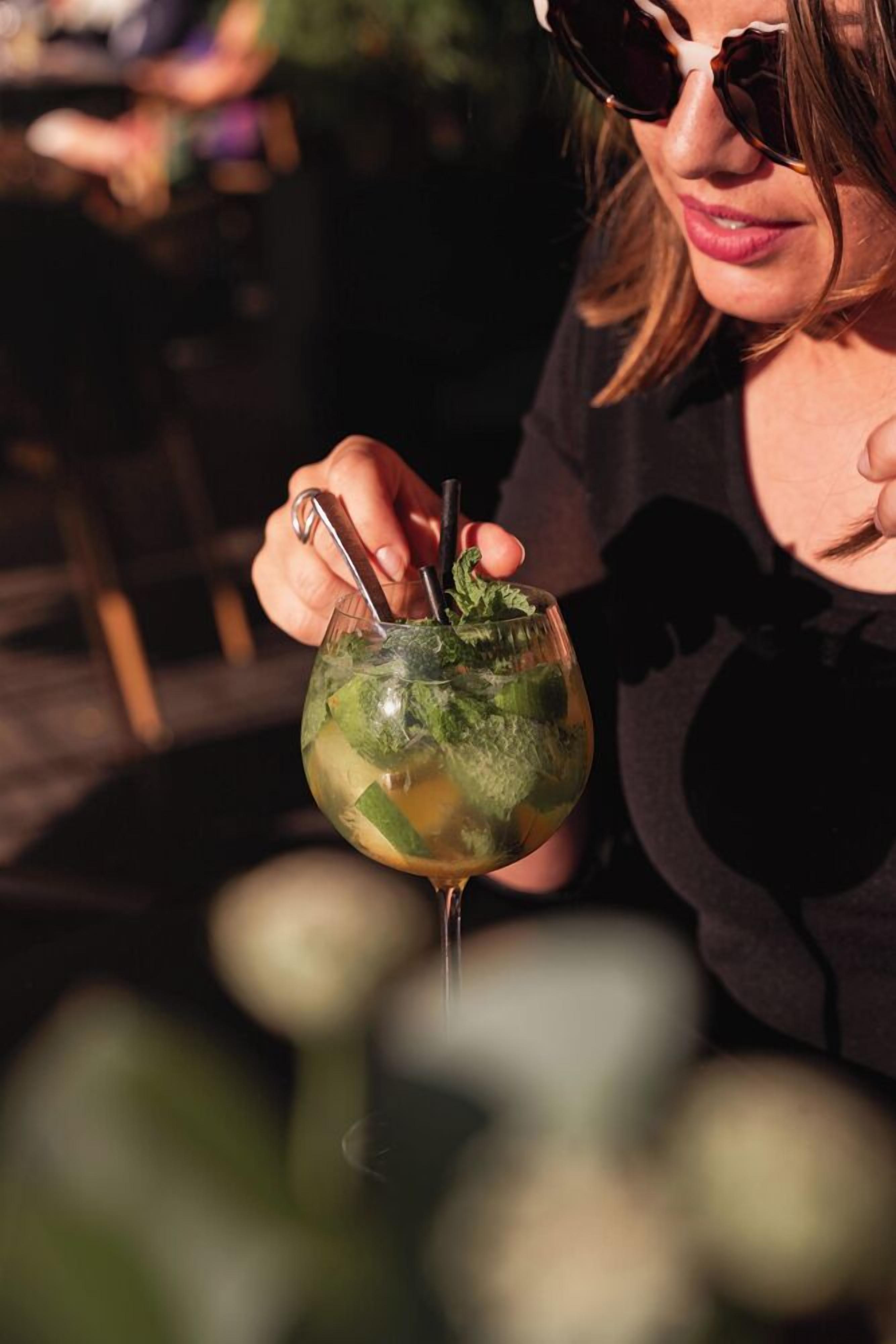 Una persona sosteniendo un vaso con pajita y una ramita de menta.