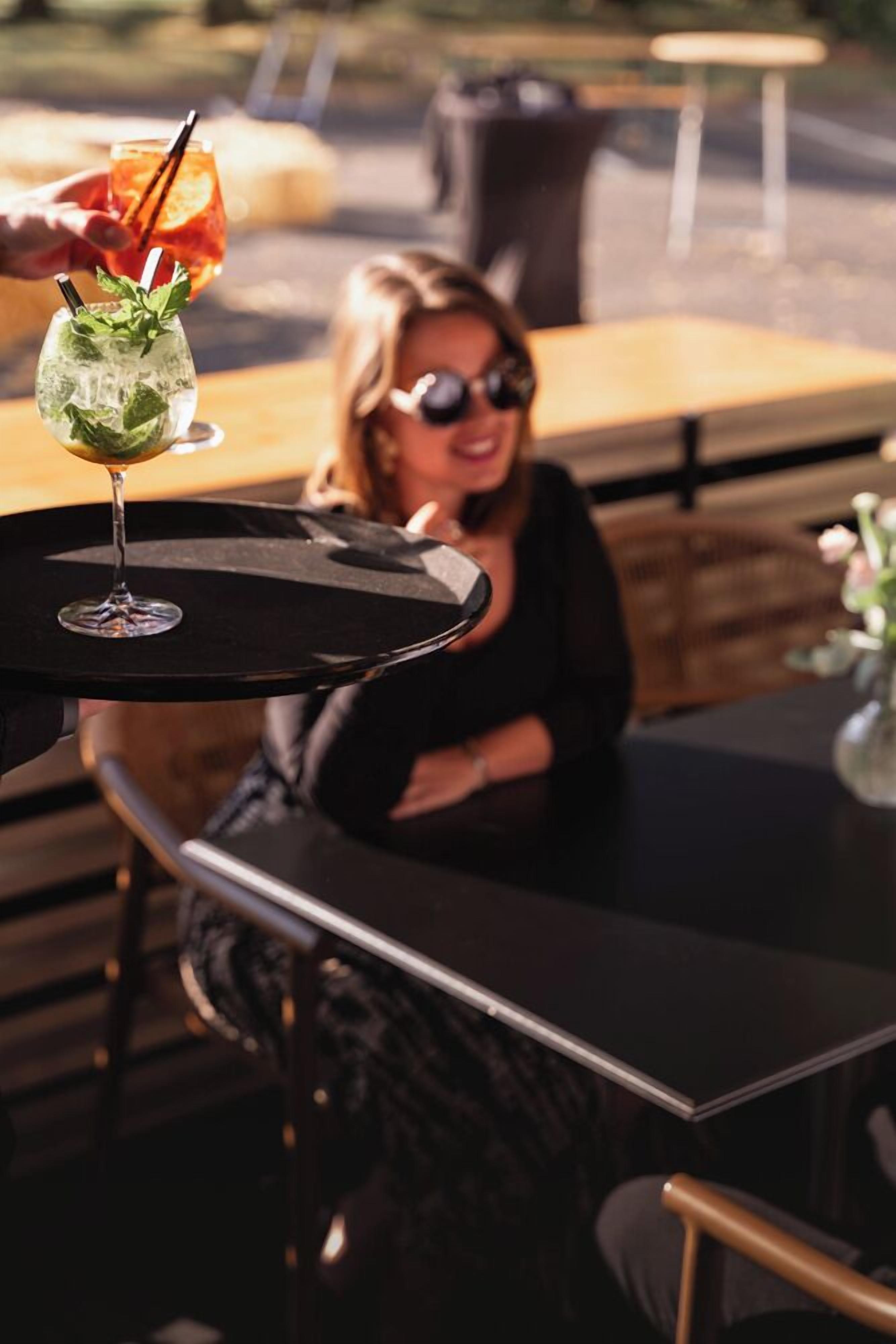 Iemand zit aan een buitentafel met een drankje en een glas water.