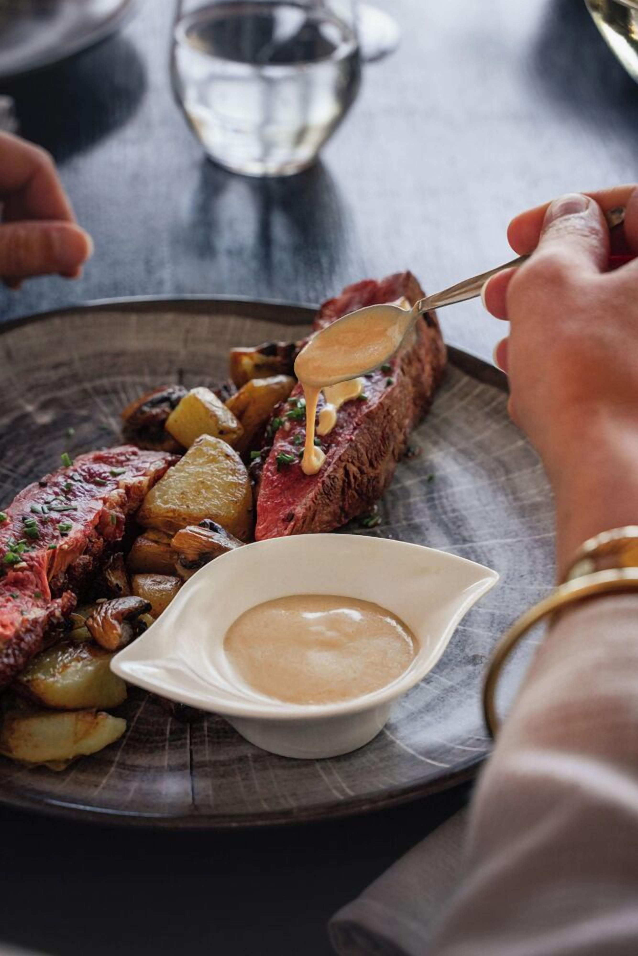 A steak with a creamy sauce and roasted potatoes on a plate.