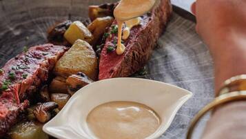 A steak with a creamy sauce and roasted potatoes on a plate.