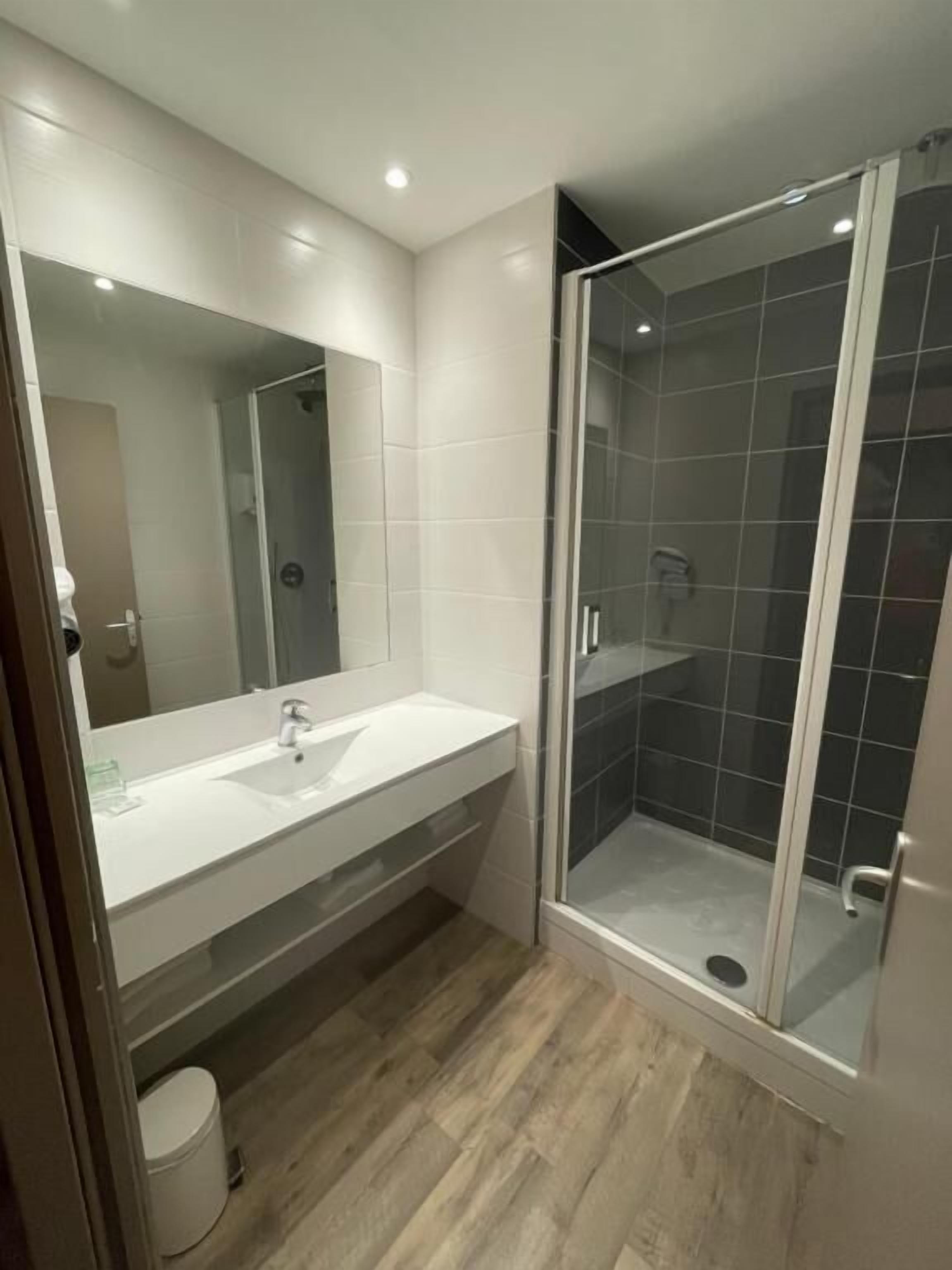 Un bagno moderno con un mobile lavabo bianco, uno specchio grande e un'area doccia con pareti in vetro.