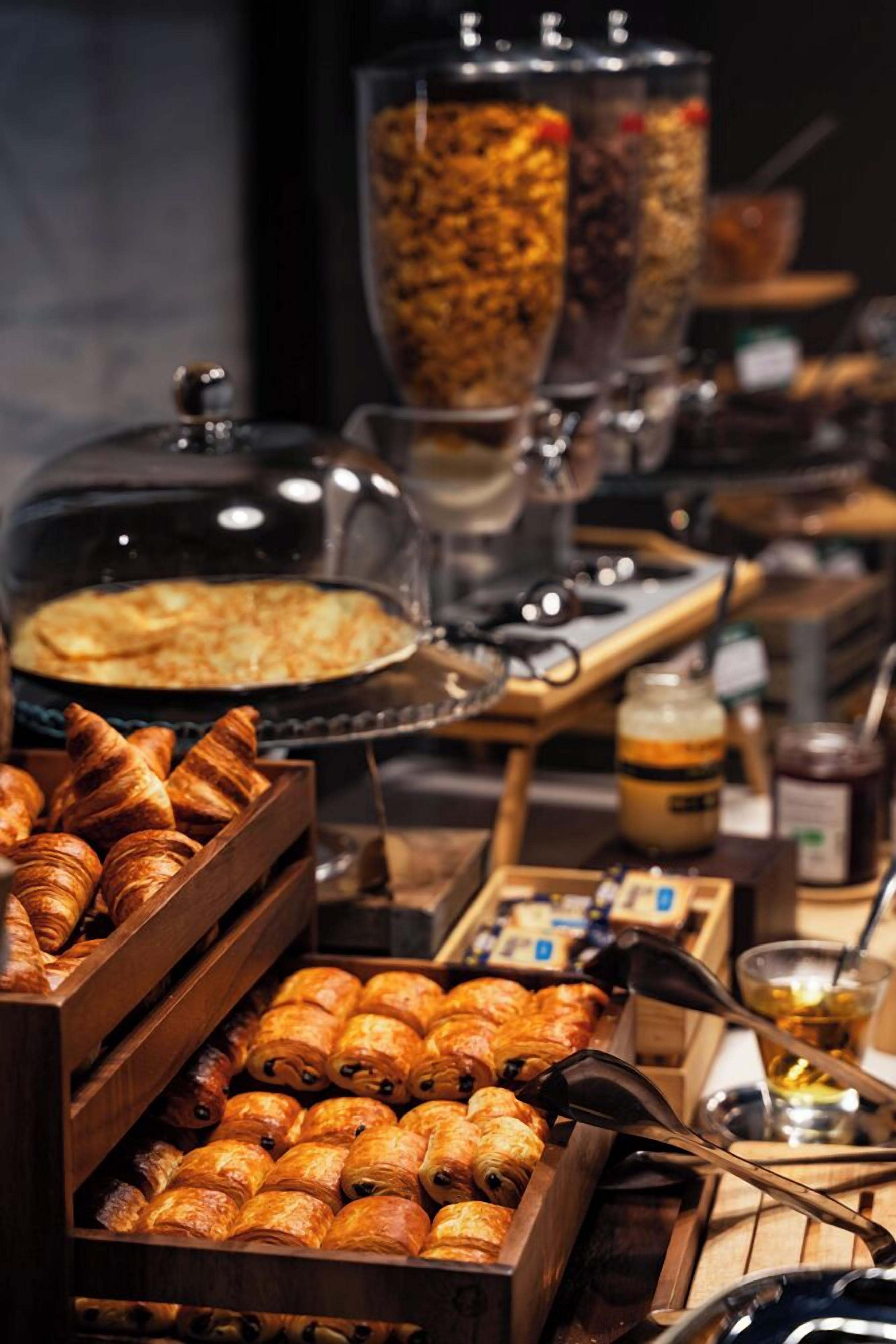 Un bufé con diversas opciones de panadería, incluyendo cruasanes y un recipiente tapado, probablemente con pasteles o postres.