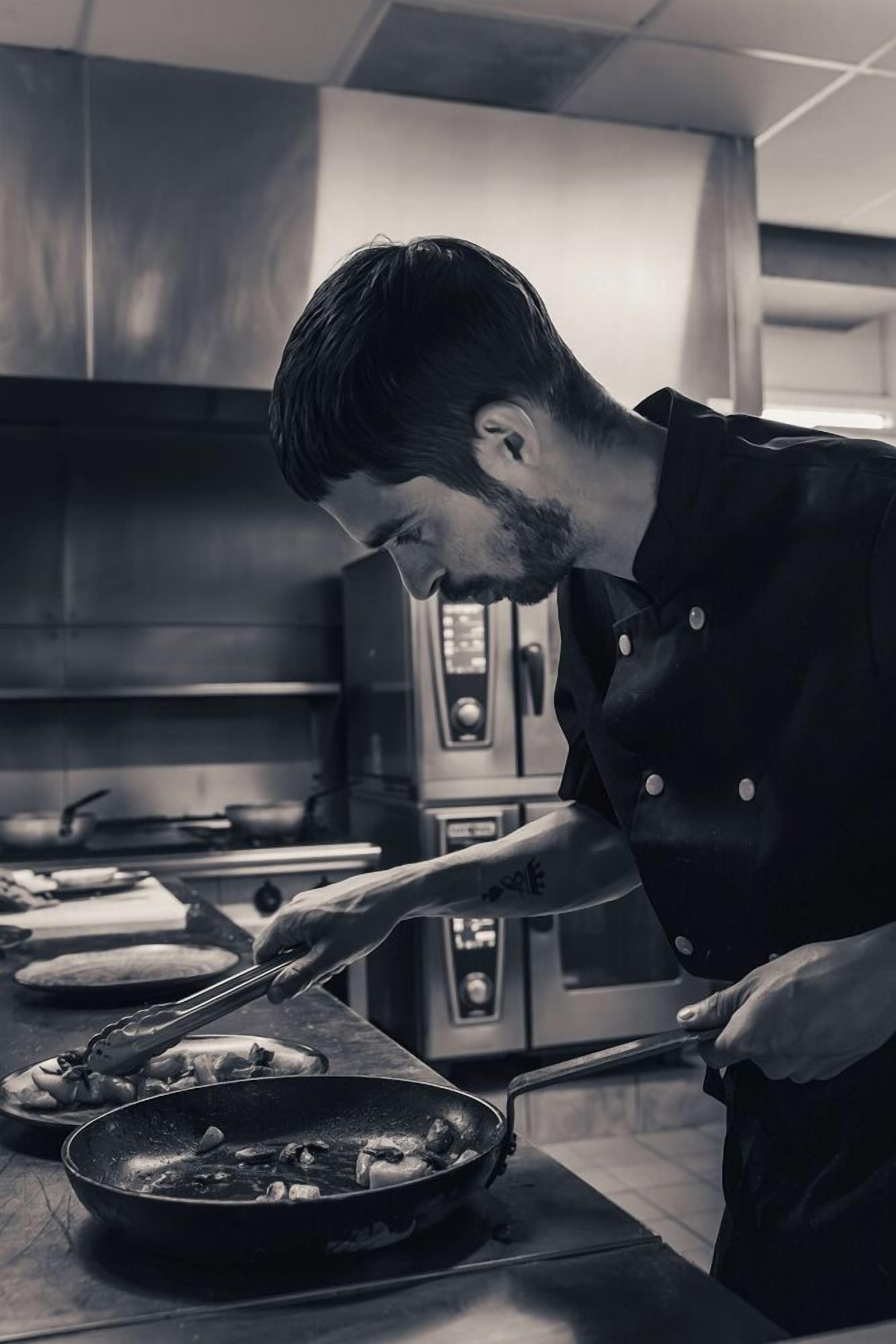 A chef cooking in a professional kitchen with stainless steel appliances and a clean, organized layout.