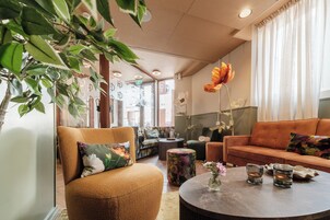 Una sala de estar acogedora con un sofá, un sillón y una mesa de centro, con una planta grande y un jarrón con flores.