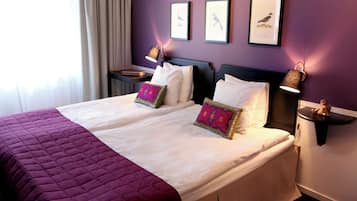 A double bed with a purple quilt, two bedside tables with lamps, and framed bird pictures on the wall.