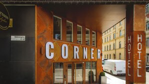 A hotel entrance with a large sign reading 'CORNER HOTEL,' a glass door entrance, and a brick-paved sidewalk. - Corner Hotel (Stockholm)