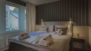 A hotel room with a large bed, a bedside table with a lamp, a window with curtains, and a view of the outside. - Corner Hotel (Stockholm)