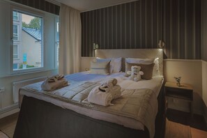 Camera d'albergo con un letto grande, un comodino con una lampada, una finestra con tende e vista esterna.