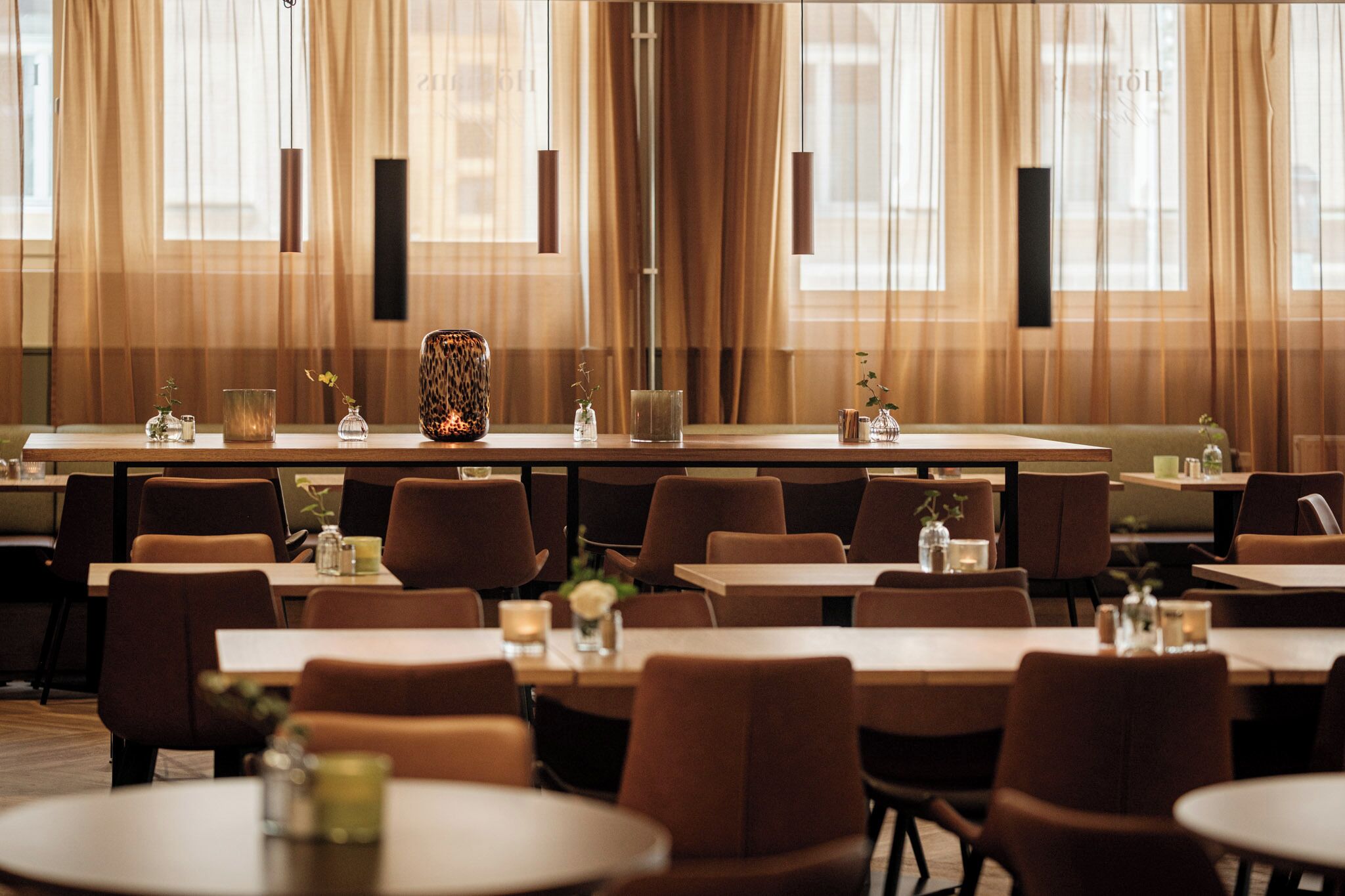 A restaurant with multiple tables and chairs, a long counter, and a vase with a plant.