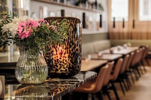 A restaurant interior with a long dining table, chairs, a vase with flowers, and a leopard print container. - Corner Hotel (Stockholm)