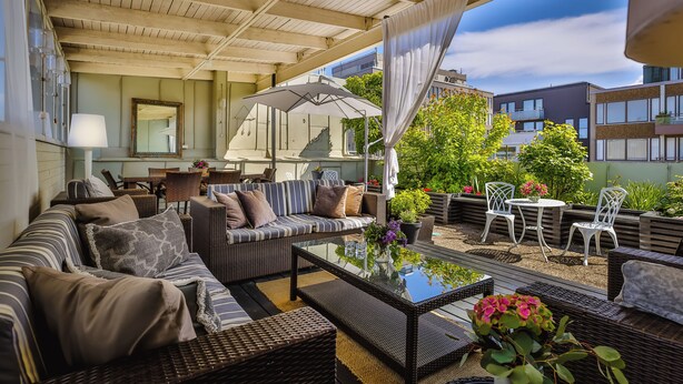 A covered outdoor seating area with wicker furniture, a glass table, and potted plants. - Corner Hotel (Stockholm)