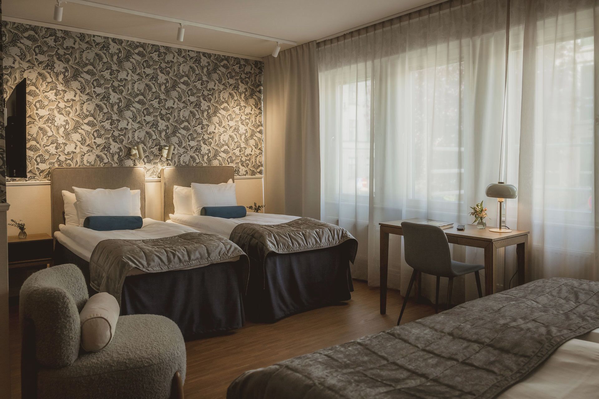 A hotel room with two beds, a desk, a chair, and a couch.