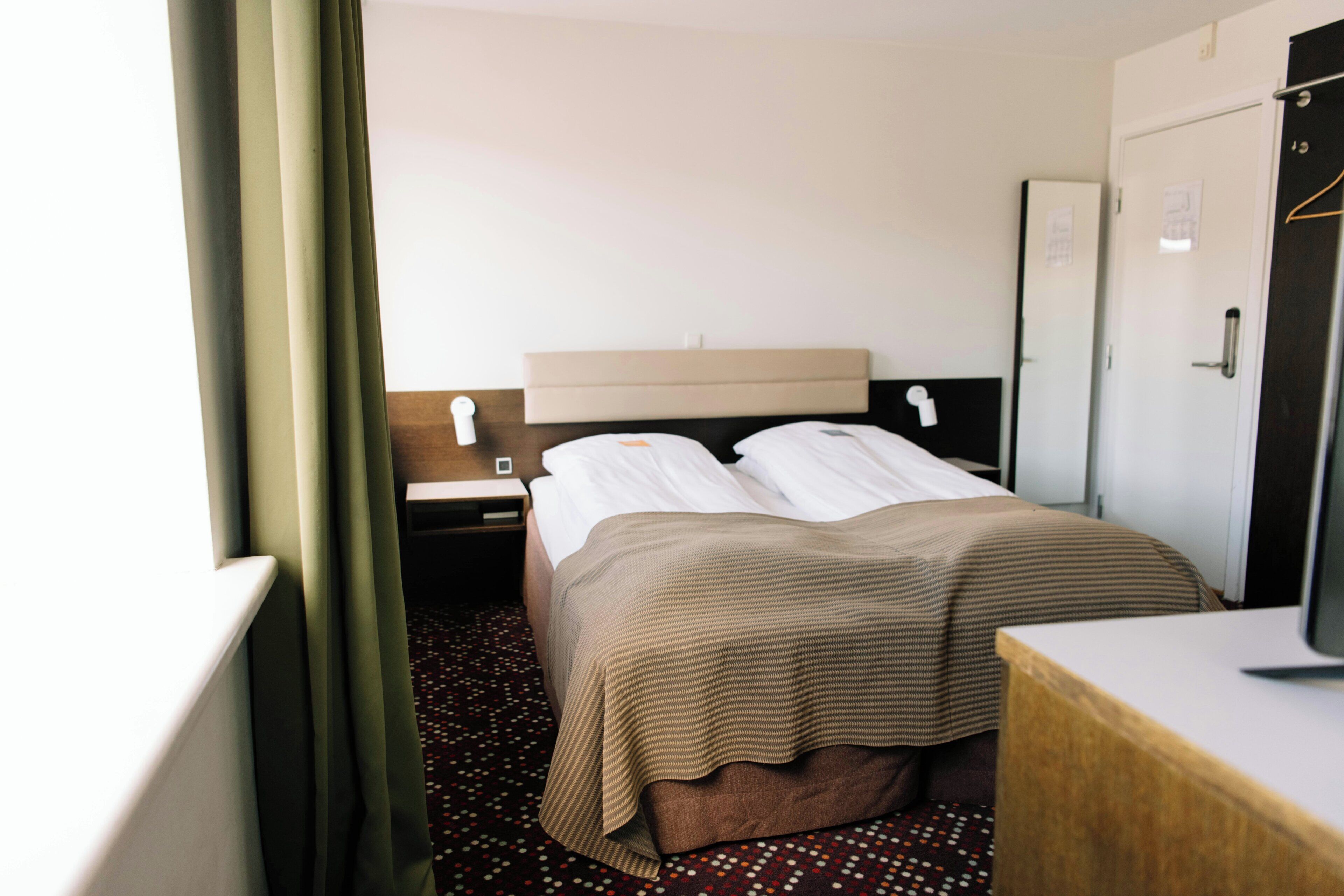 A hotel room with a bed, a nightstand, a desk, and a wardrobe.