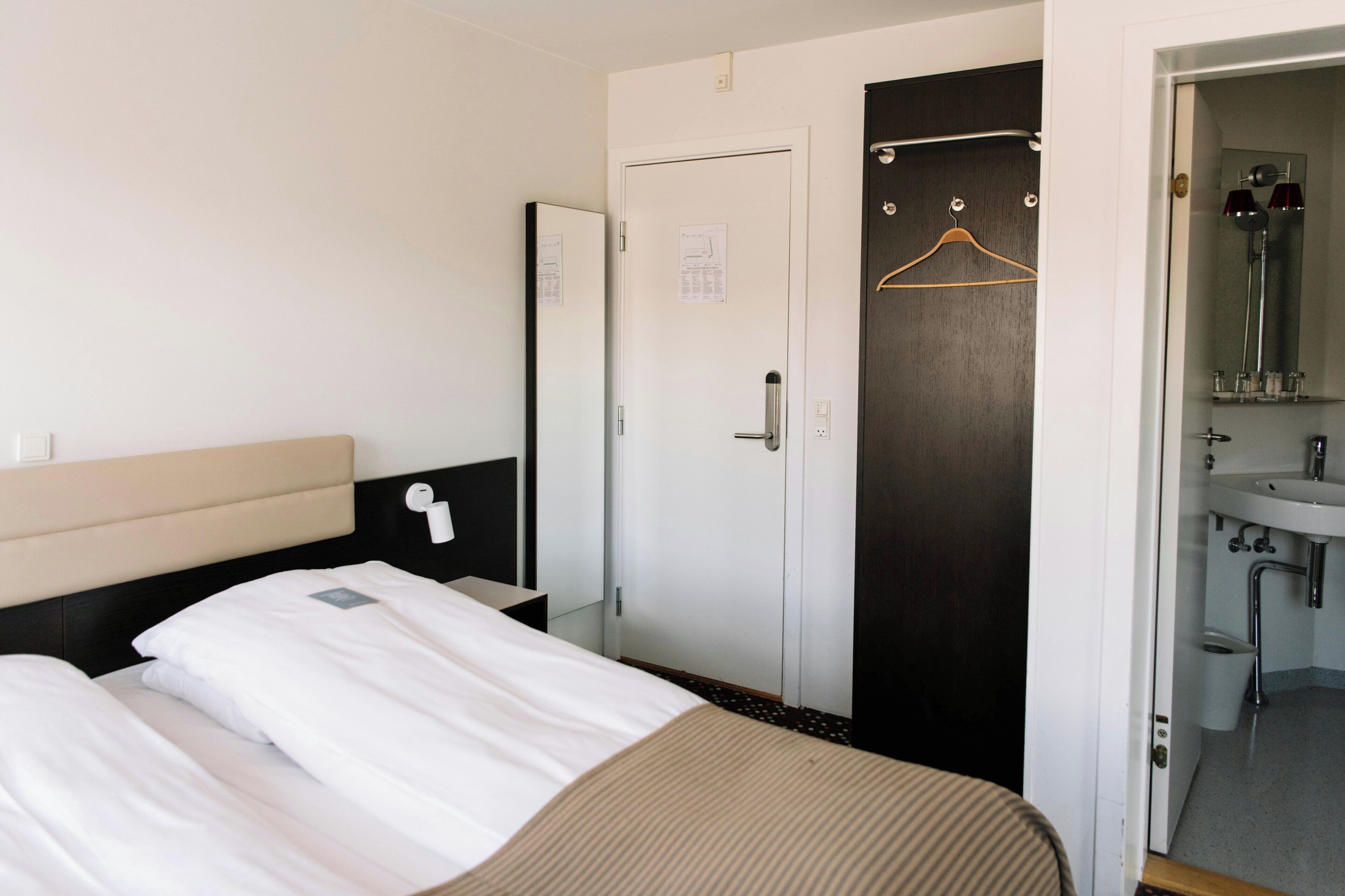 Une chambre d’hôtel avec un lit, une armoire, une salle de bain avec un miroir et un lavabo.