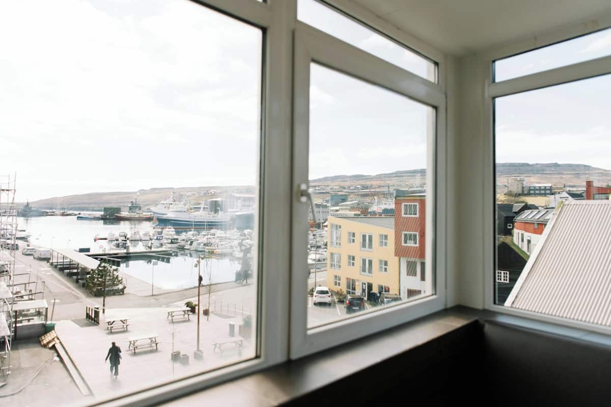 A view from a window overlooking a marina with boats, a pedestrian walkway, and buildings.