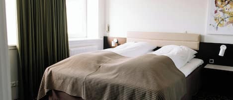 A hotel room with a bed, a window with curtains, a wall-mounted nightstand, and a painting.