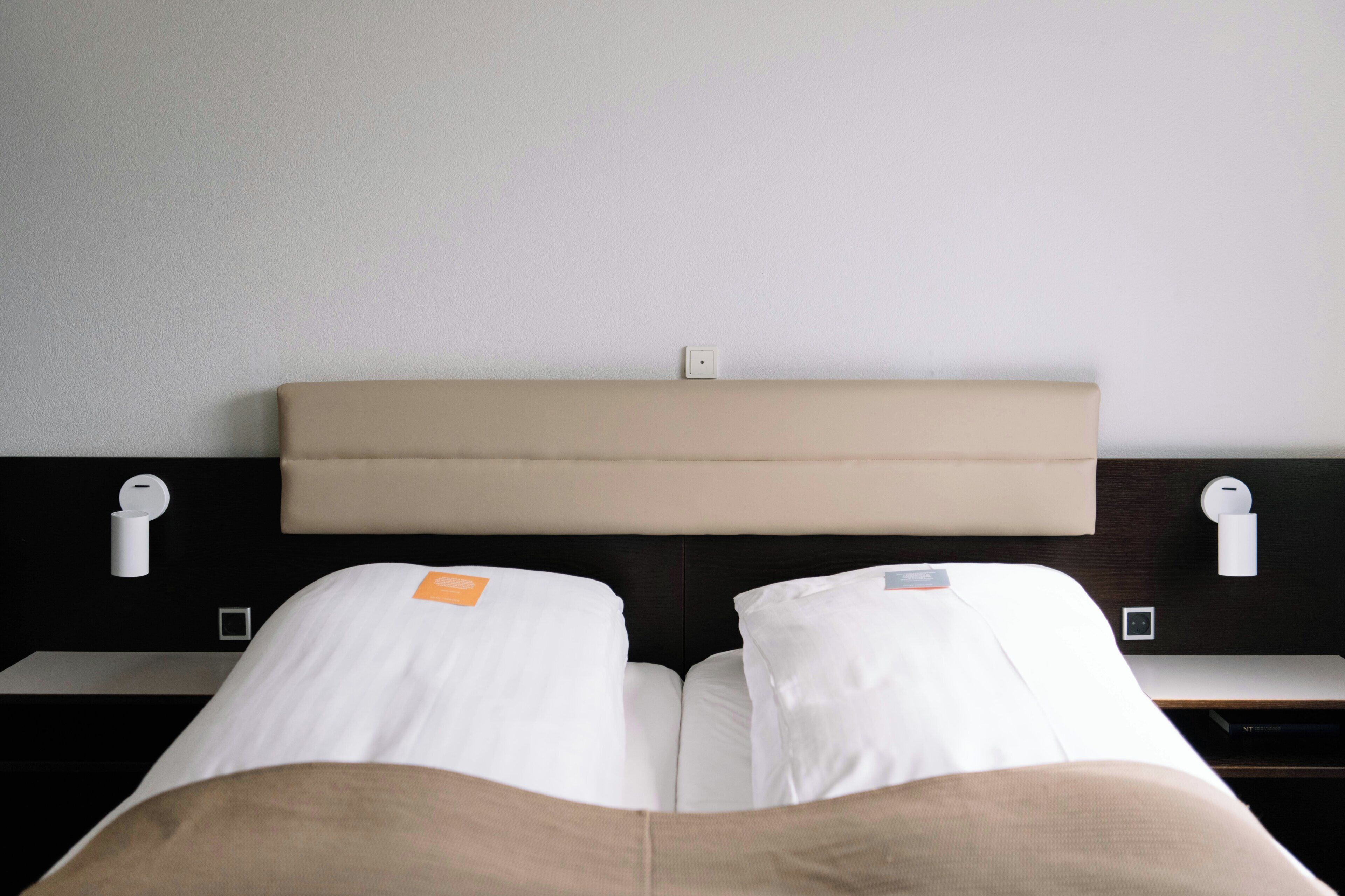 A hotel room with a bed, a headboard, bedside tables, and wall-mounted charging stations.