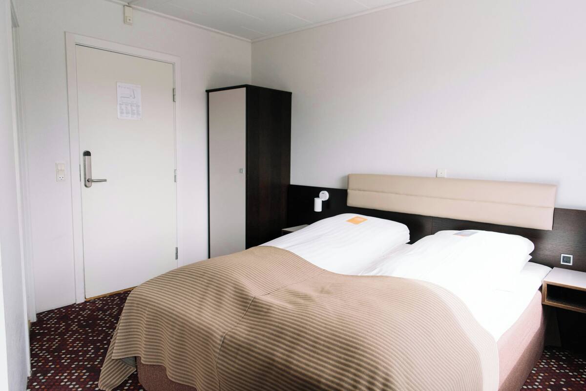 A hotel room with a bed, a wardrobe, a nightstand, and a door.