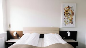 Hotellihuone, jossa on sänky, kaksi yöpöytää, seinälle ripustettu taideteos ja ikkuna.