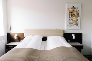 Habitación de hotel con cama, dos mesitas de noche, una obra de arte en la pared y una ventana.