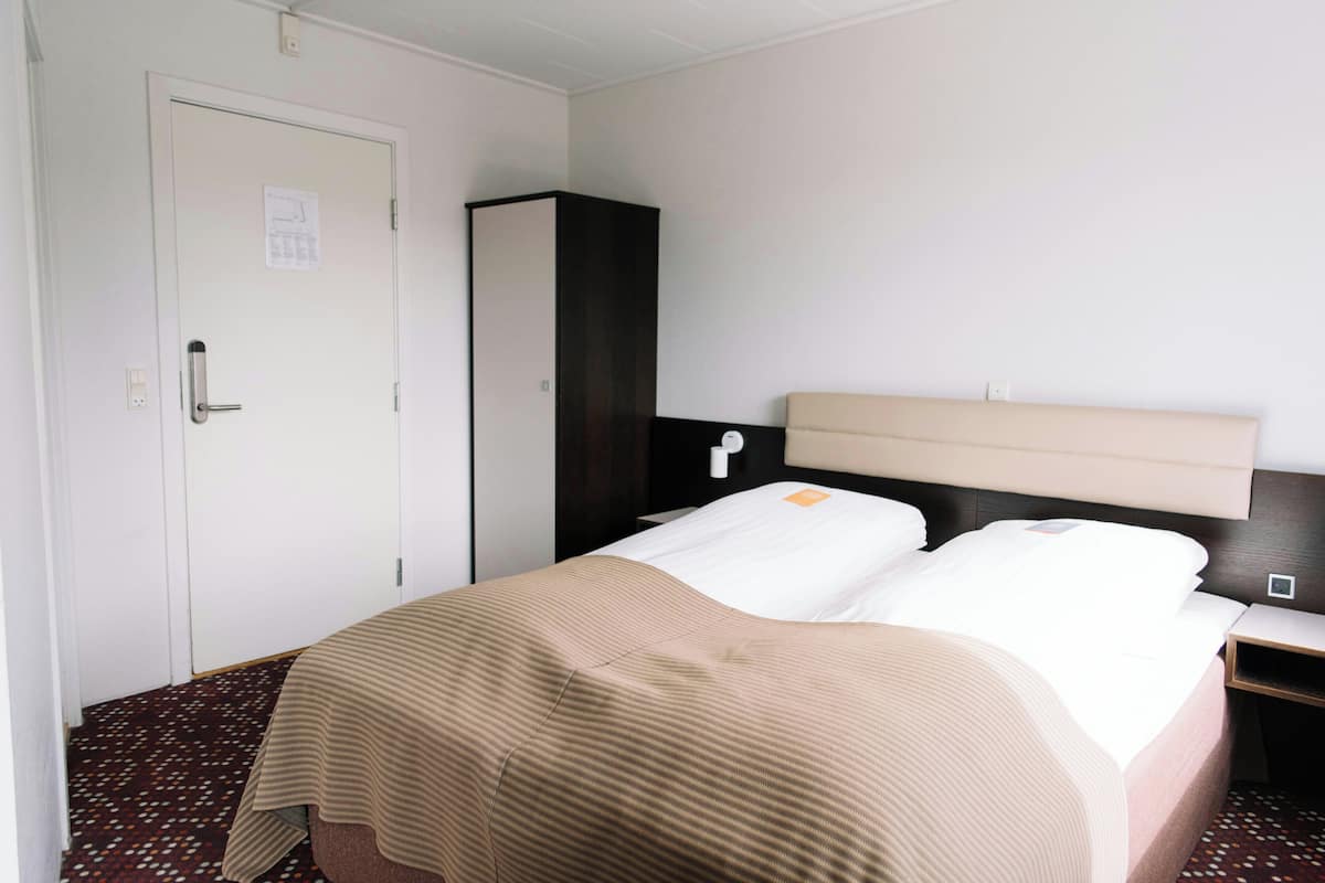 A hotel room with a bed, a wardrobe, a nightstand, and a door.