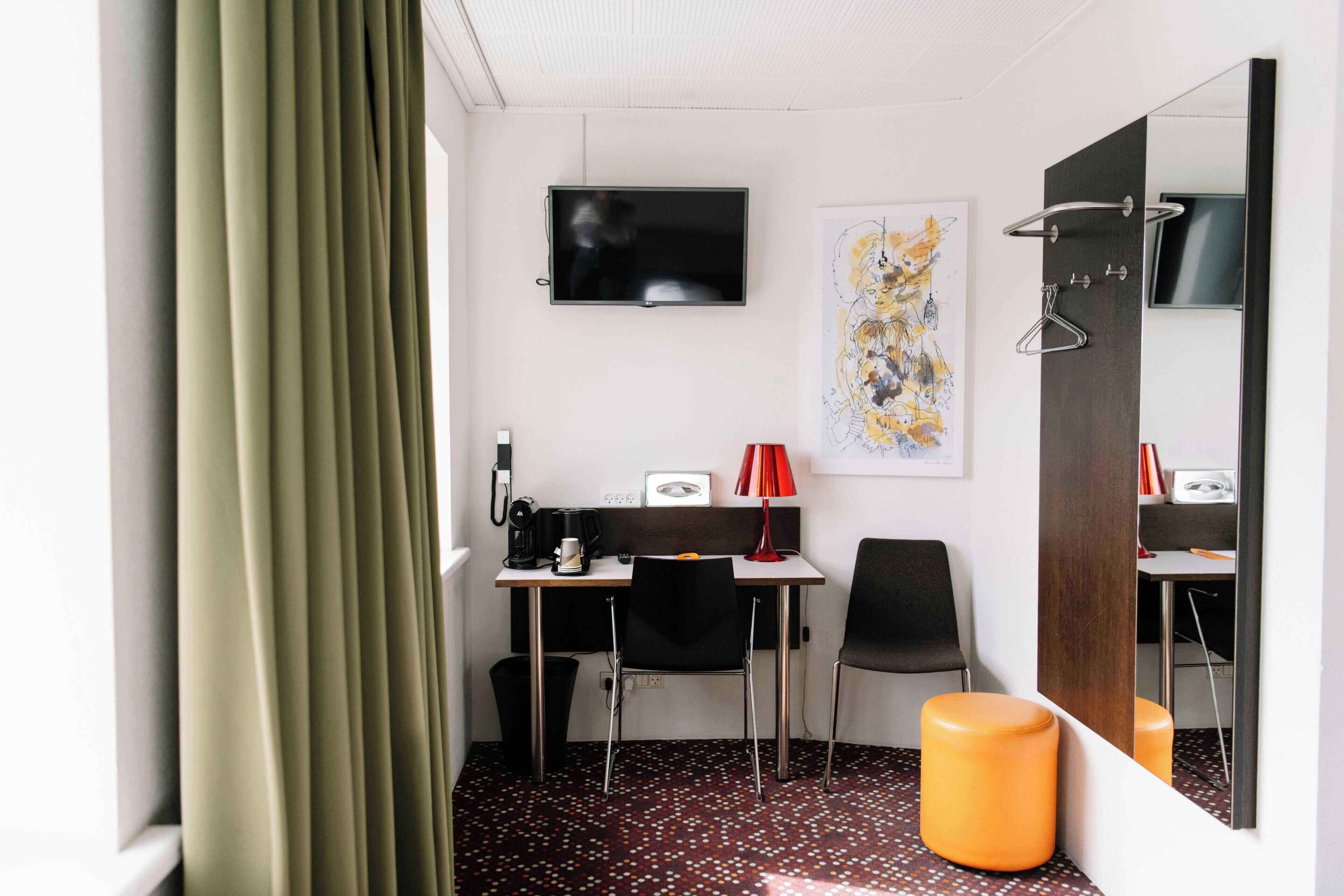A hotel room with a desk, two chairs, a television, a mirror, and a patterned floor.