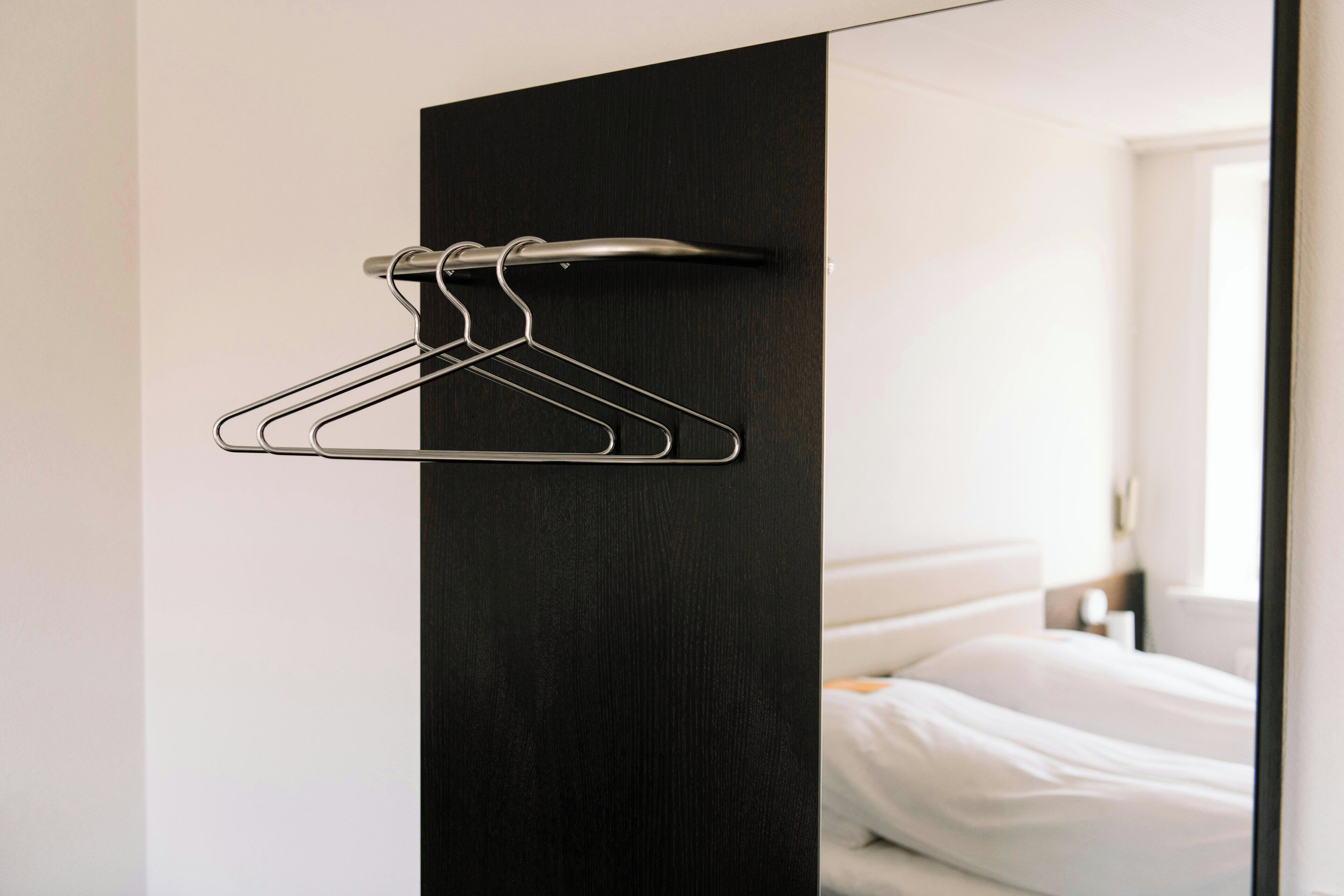 A modern hotel room with a dark wood panel, a metal hanger rack, and a neatly made bed.