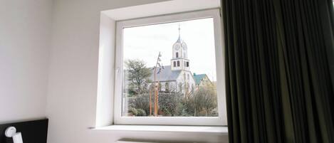 A hotel room with a large window, a radiator below, and a view of a church with a clock tower.