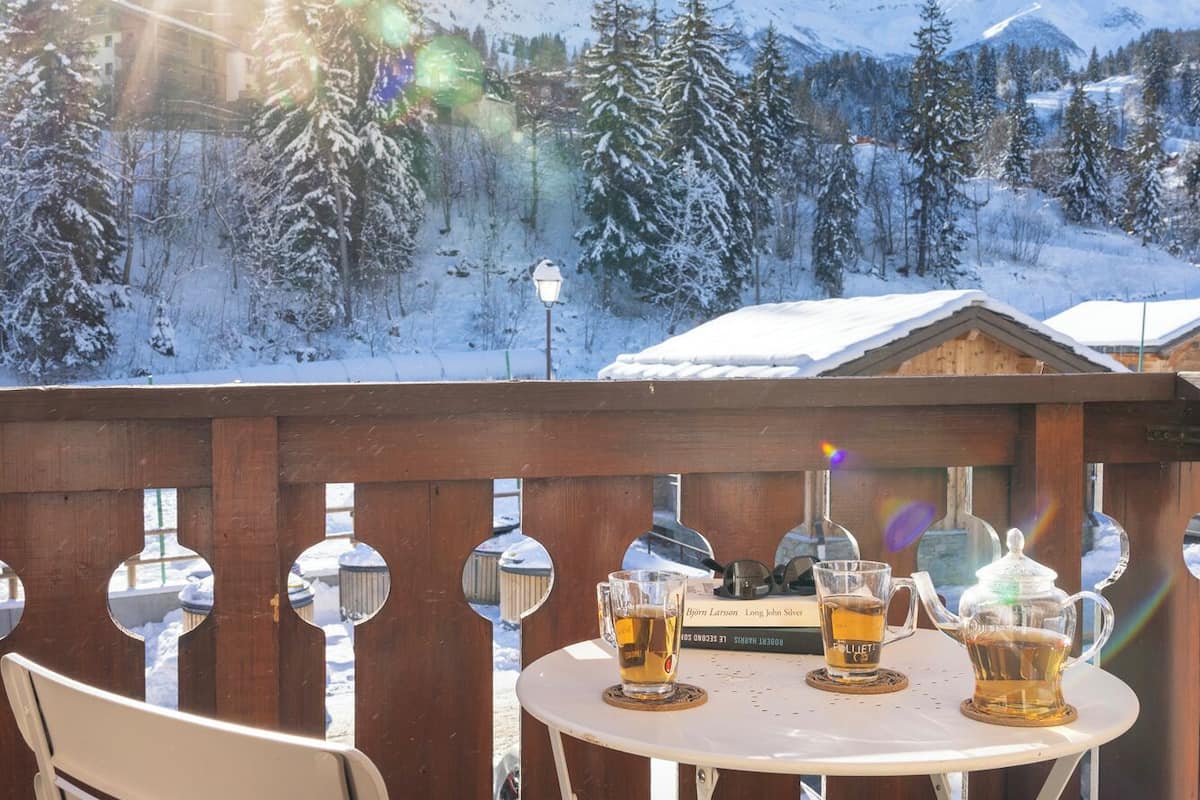 A balcony with a table set for two, overlooking a snowy mountain landscape.