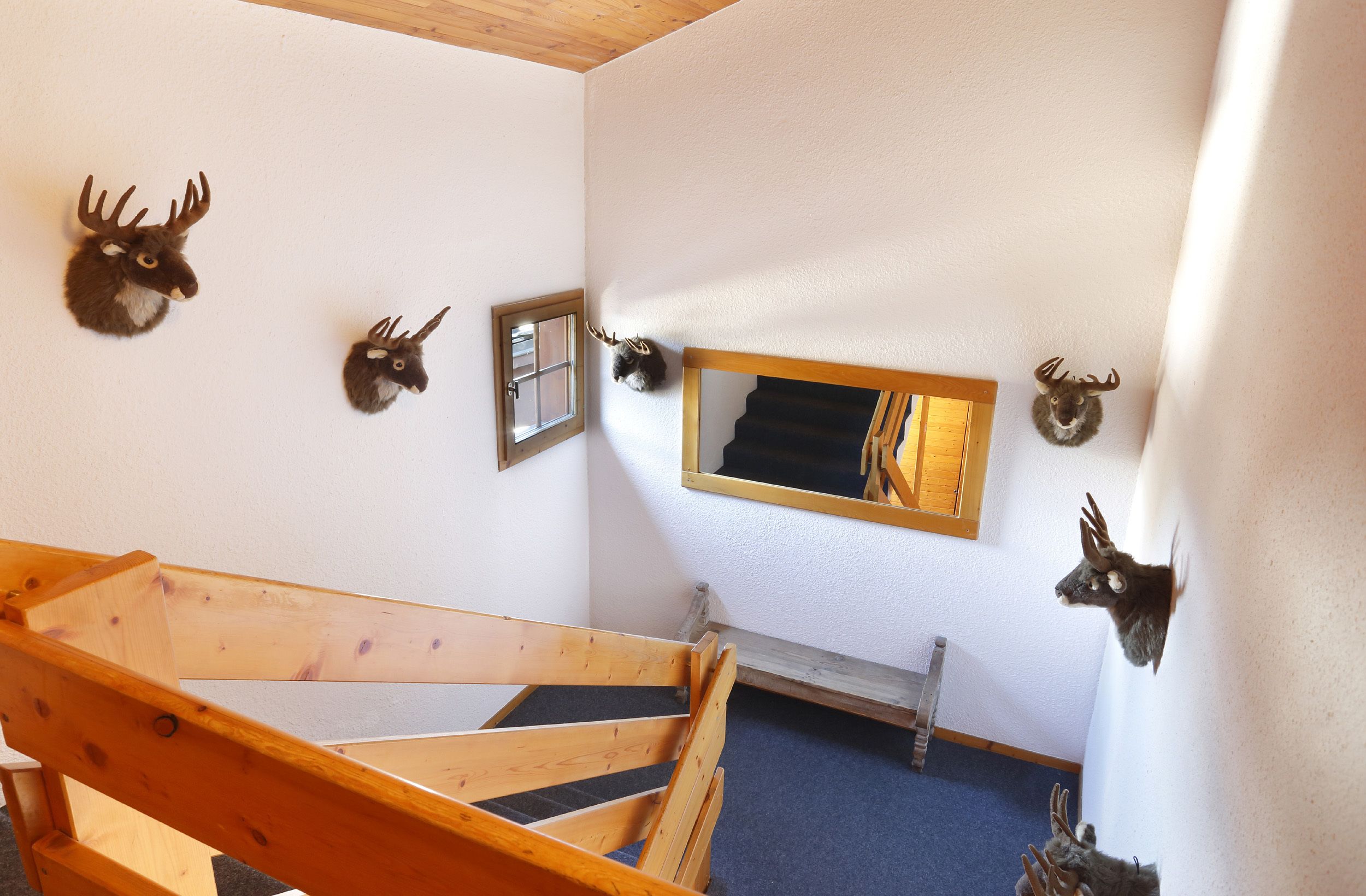 Una habitación con una escalera de madera, un espejo y varias decoraciones de cabeza de ciervo en las paredes.