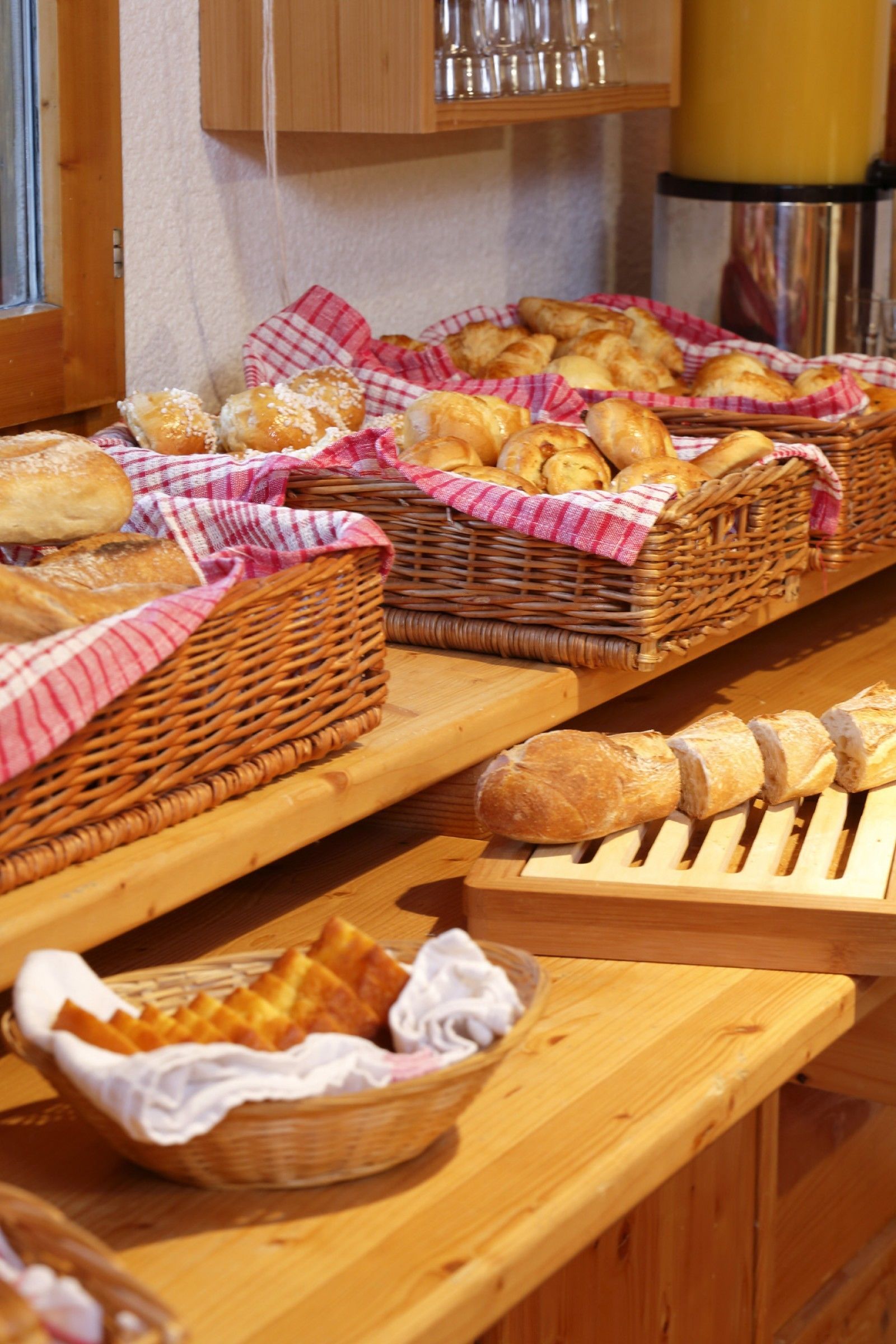 Uma mesa de buffet com diversos pães e doces dispostos em cestos de vime e bandejas de madeira.